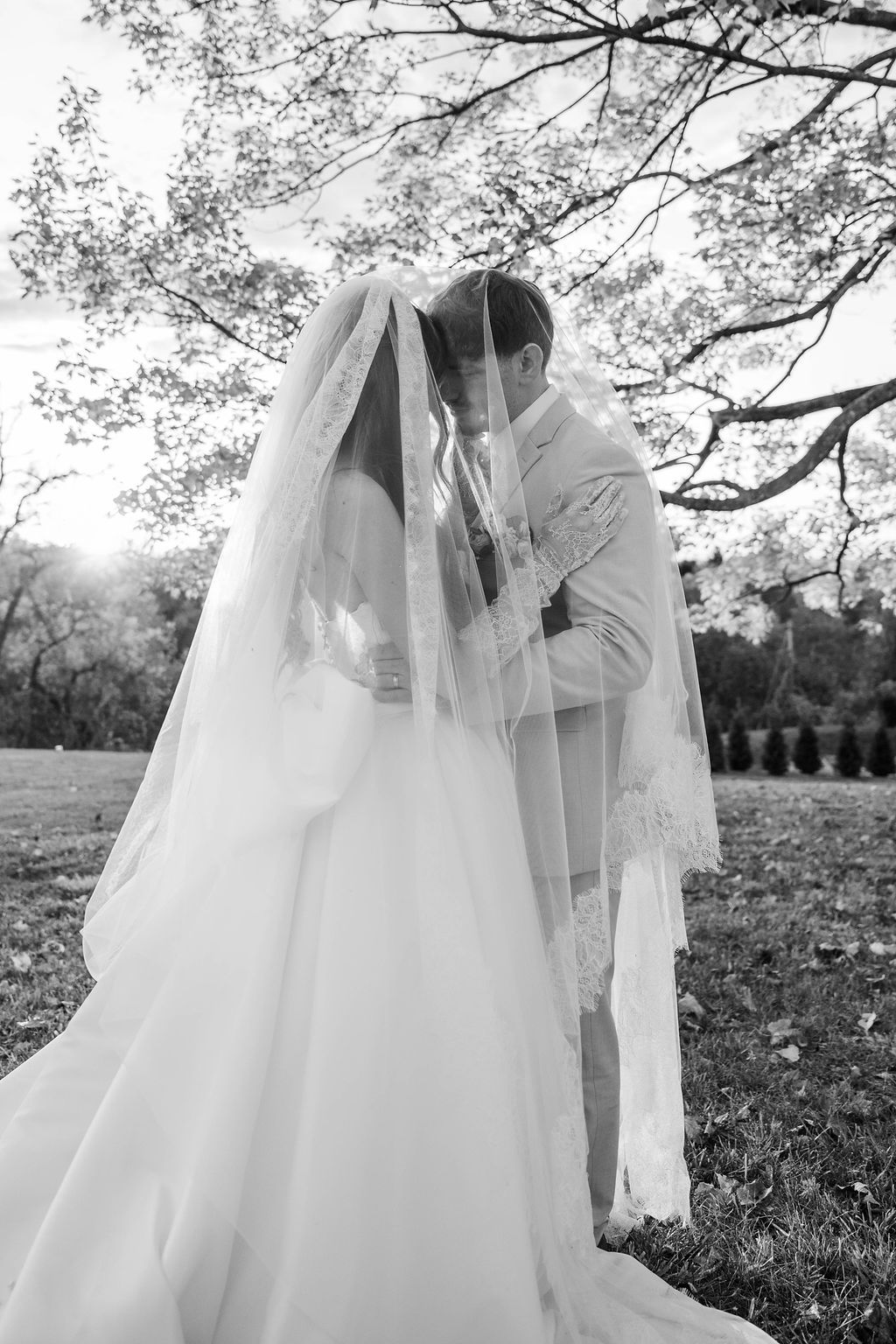 Bride and groom kissing under a veil in a black-and-white outdoor wedding photo