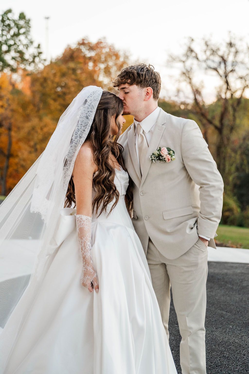 Bride and groom sharing a kiss outdoors, with autumn trees in the background