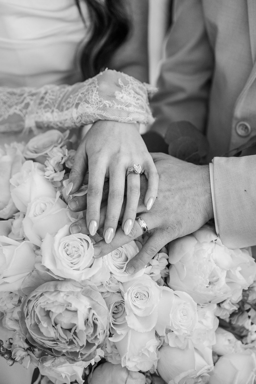Hands with wedding rings resting on a bouquet of roses and flowers in black and white