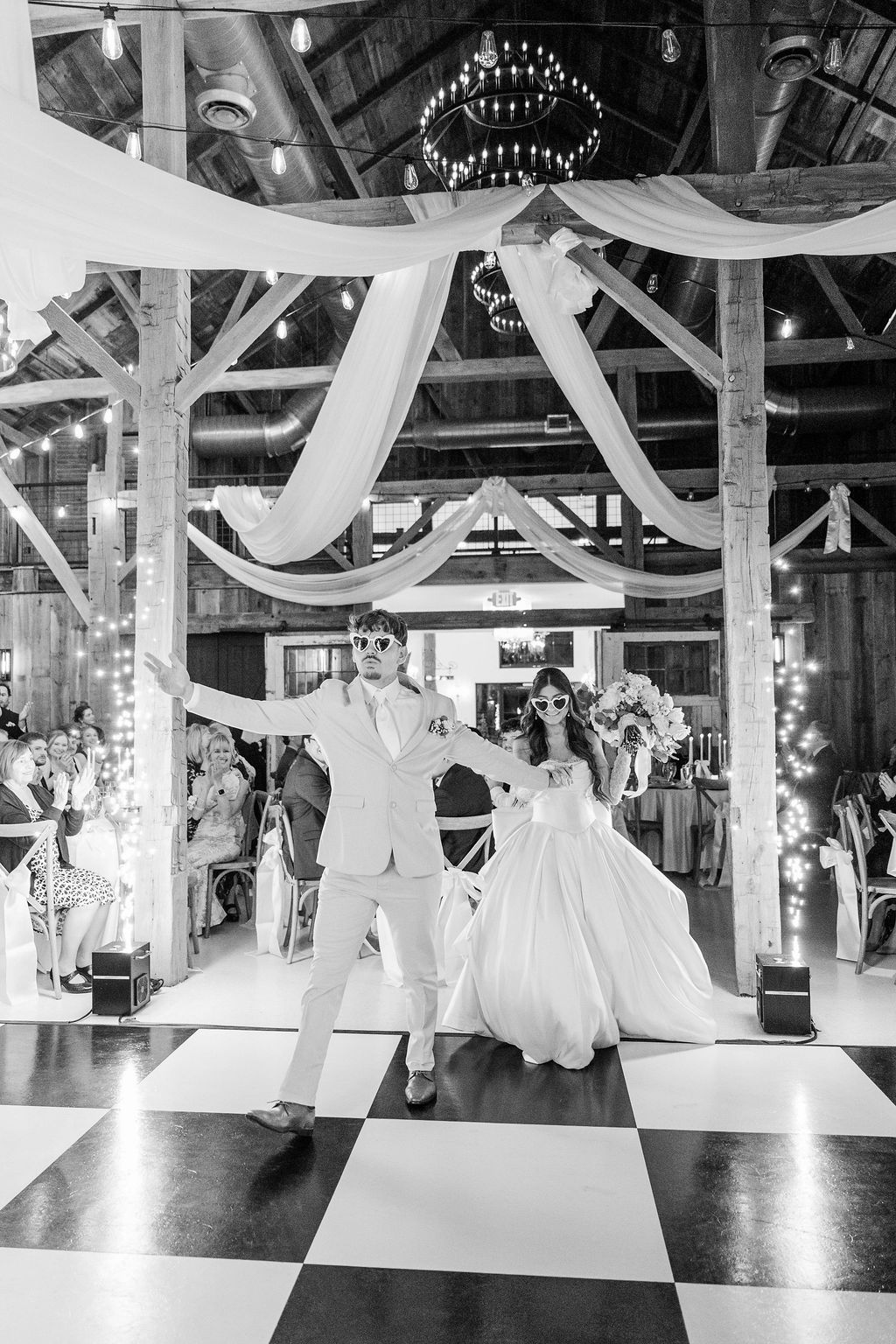 Bride and groom dancing under streamers on a checkered dance floor at a rustic wedding reception