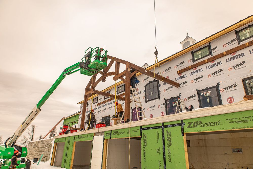 Green construction lift raises workers beside a building under renovation with exposed framing.