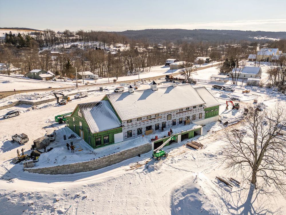 Snow-covered building under construction in a rural landscape, with green exterior walls and roof scaffolding