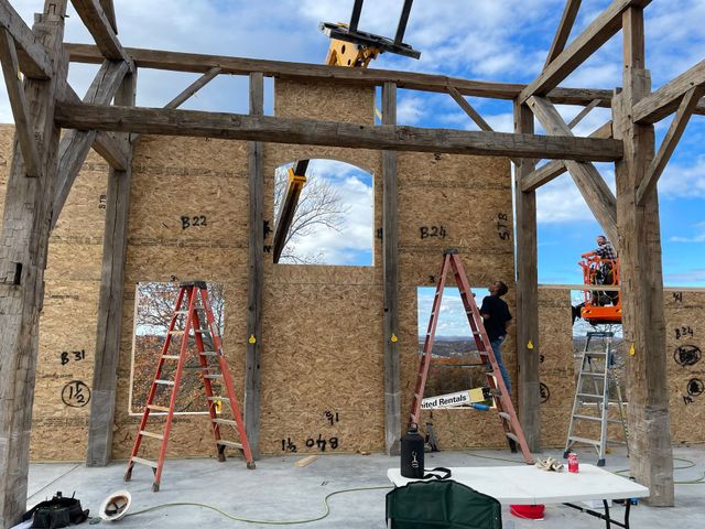 Construction of a wooden building: workers on ladders and lift, OSB wall with window frames.