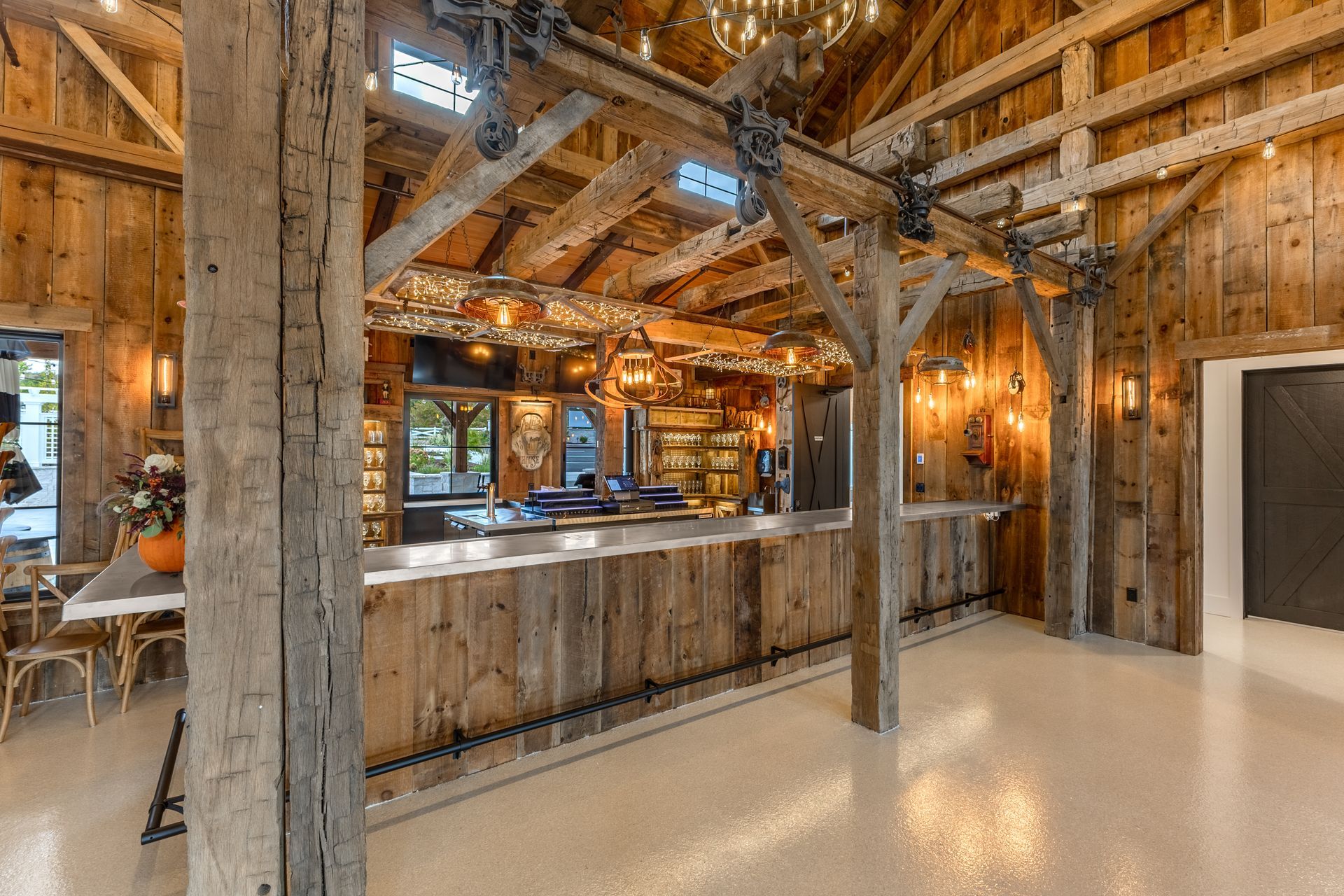Rustic wooden bar inside a barn with a glossy white floor, exposed beams, and hanging lights.
