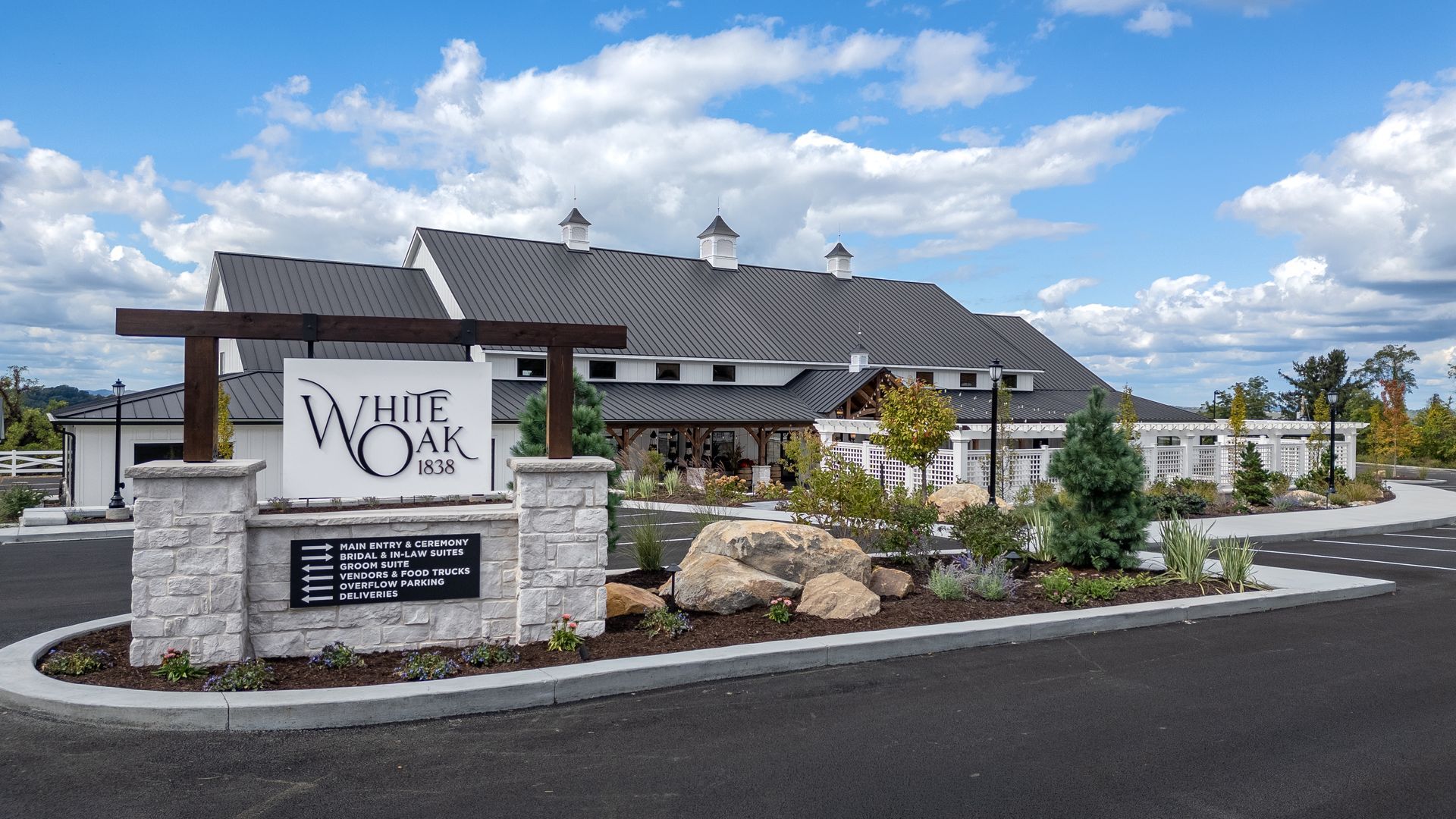 Stone sign for White Oak winery in front of a large building under a partly cloudy blue sky.