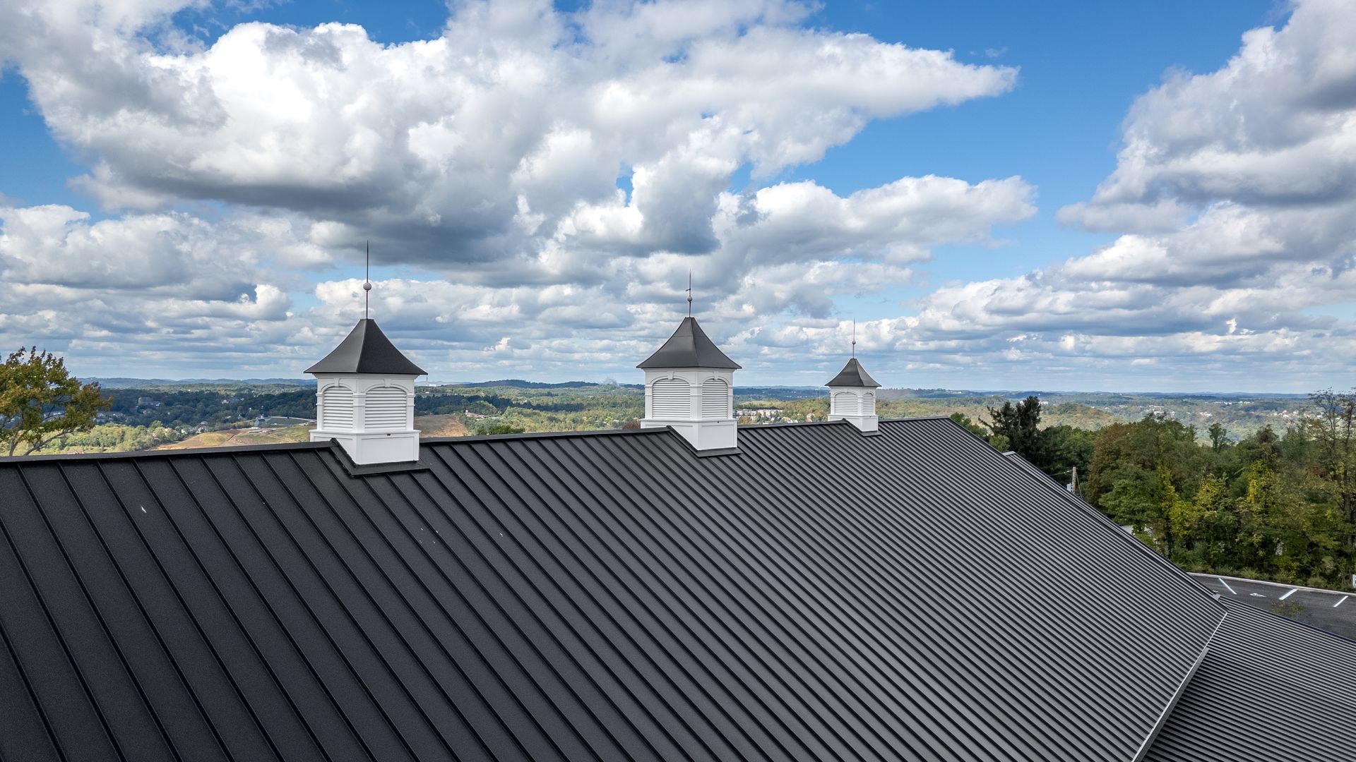 Corrugated dark roof with two white chimneys beneath a cloudy blue sky over a distant landscape
