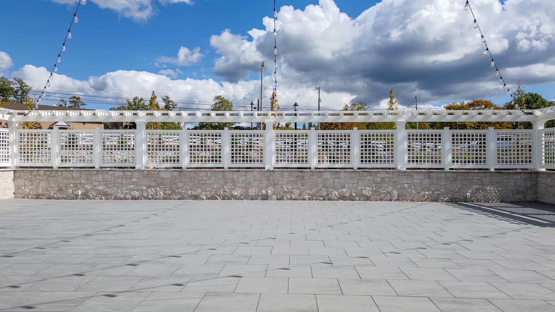 White patterned fence beside a paved plaza under a bright blue sky with large clouds