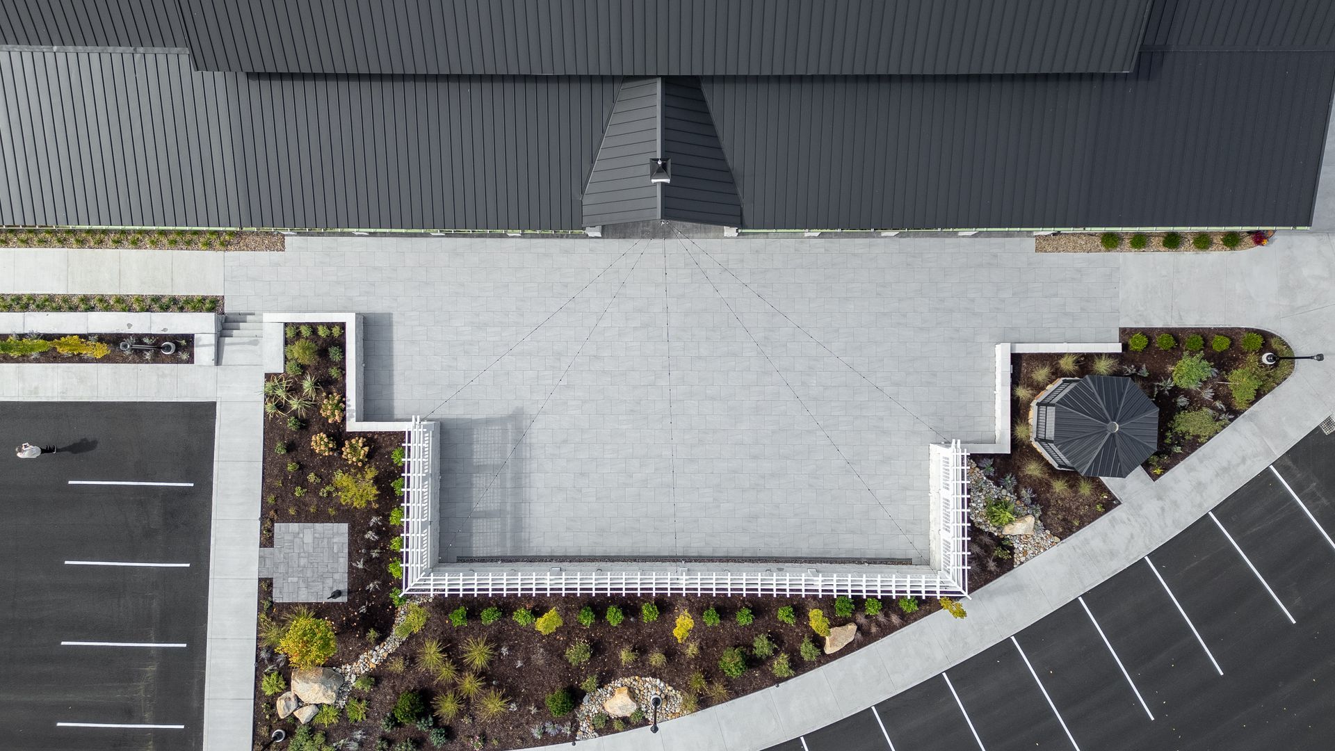 Top-down view of a modern building entrance with a paved forecourt, parking spaces, and landscaped planters