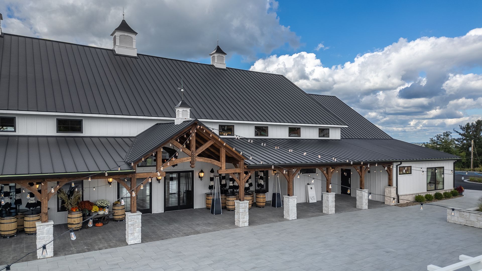 Rustic white barn-style building with dark roof, wooden porch, and flower pots under a cloudy sky