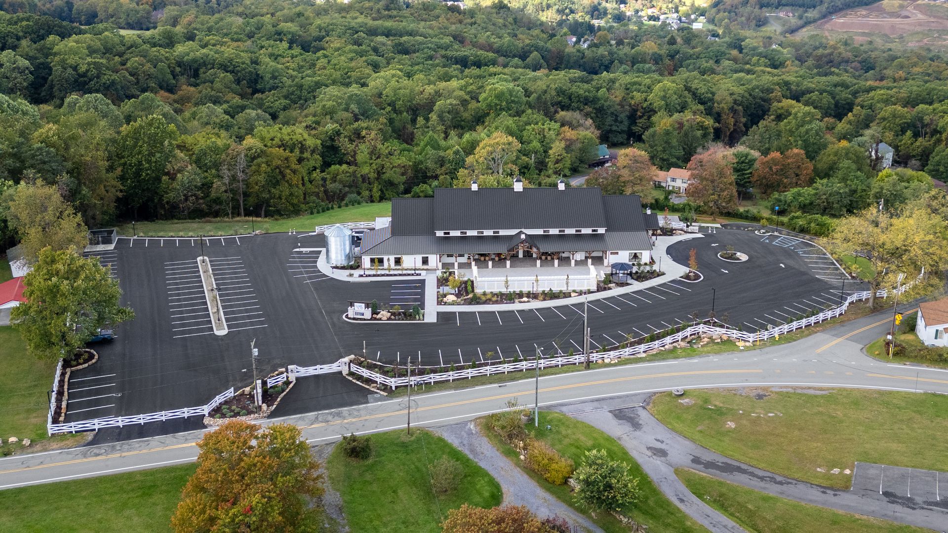 Aerial view of a large building with a mostly empty parking lot, surrounded by trees and greenery.
