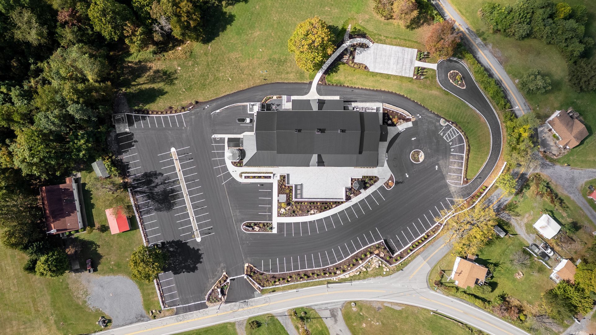 Aerial view of a large building with parking lot, cars, and surrounding trees.