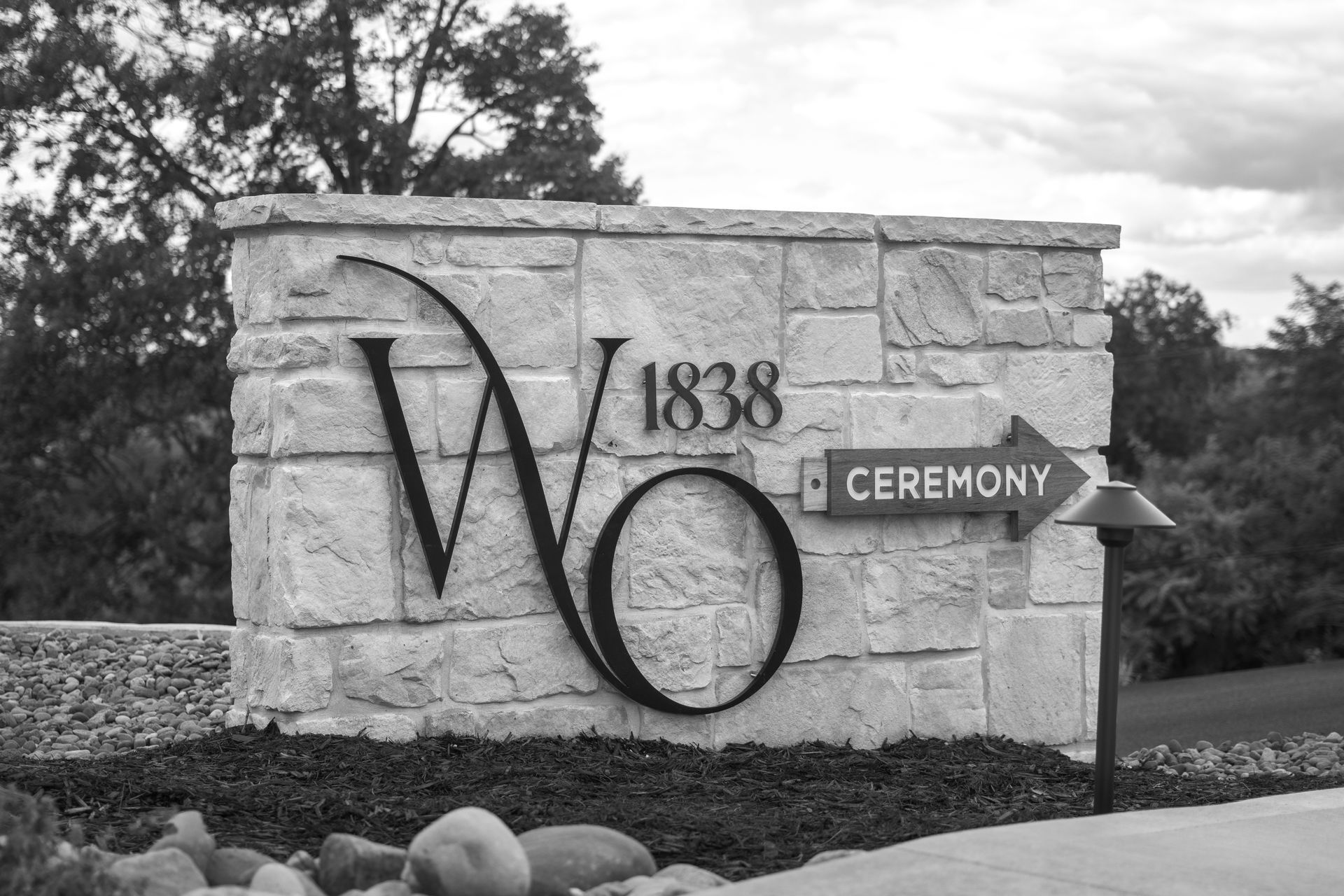 Stone entrance sign for Wooster: “1838 WO,” with a “Cemetery” arrow and trees in the background.