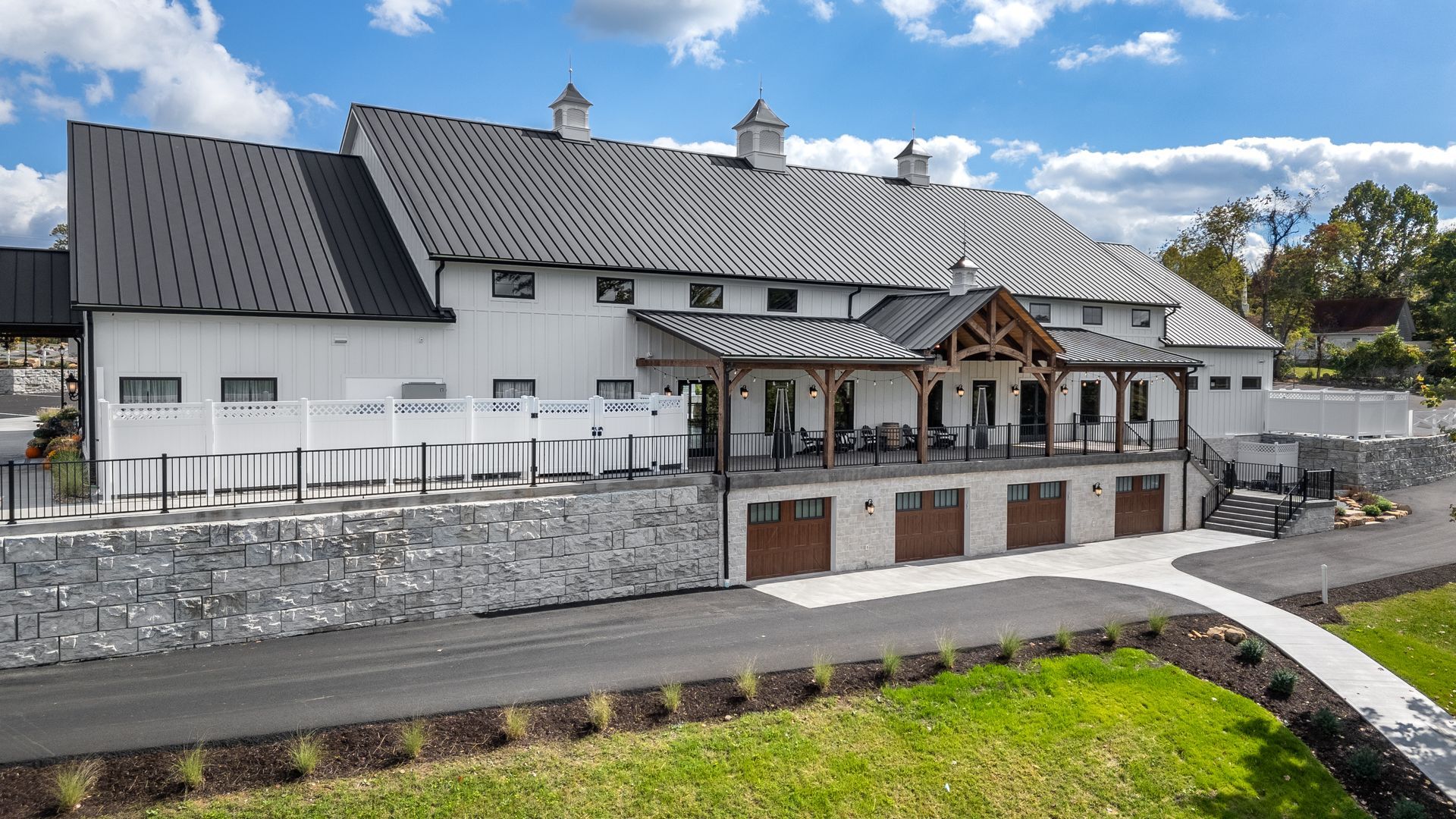 White mountain lodge with dark roof and stone wall beside a road under cloudy sky