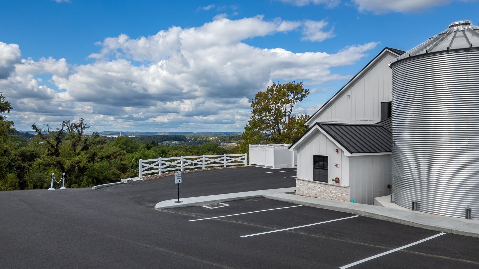 Empty parking lot beside a white building with bold black stripes under a blue, cloudy sky
