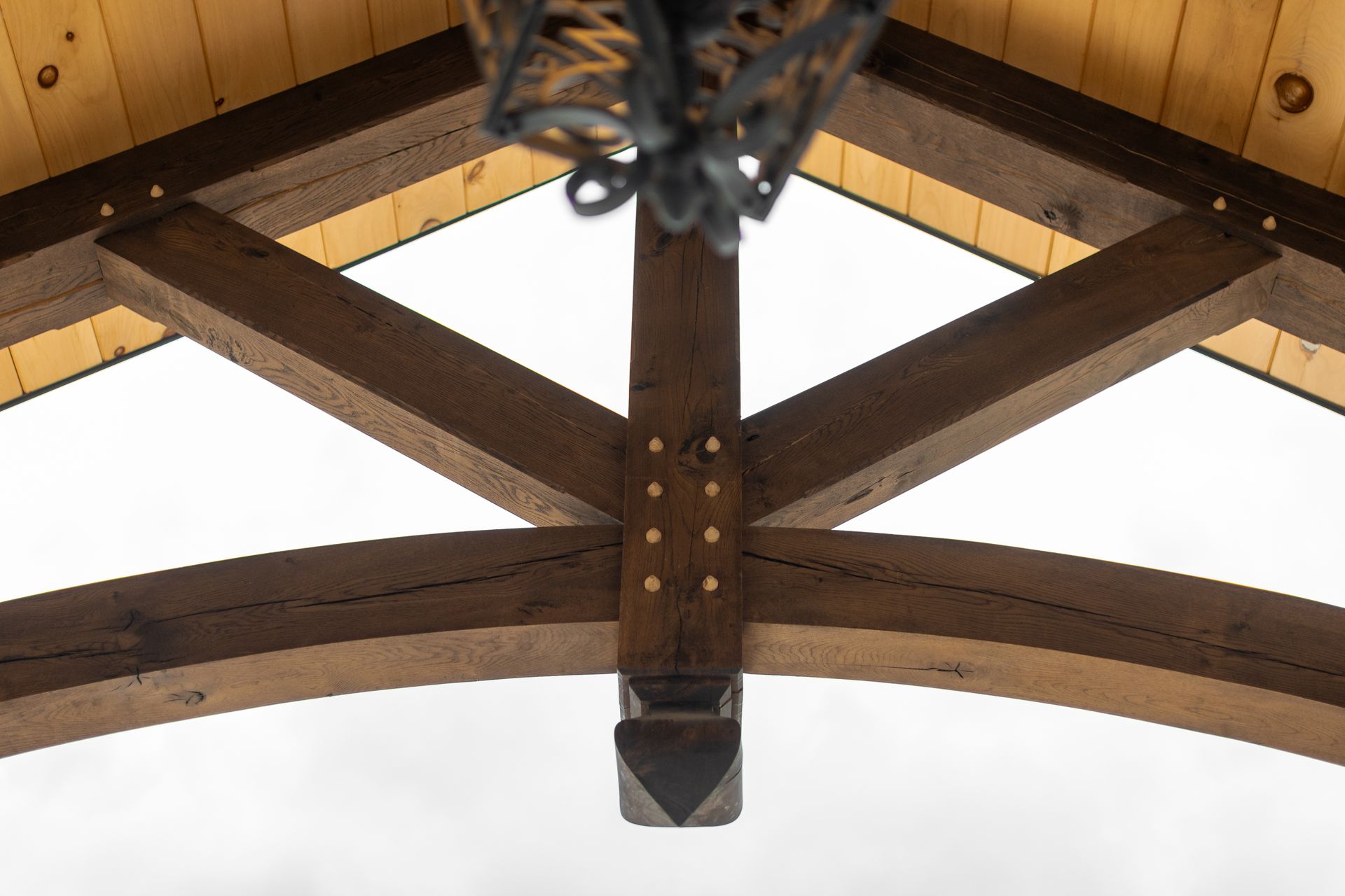 Wooden ceiling beams with bolts, forming a rustic truss against a bright white background.