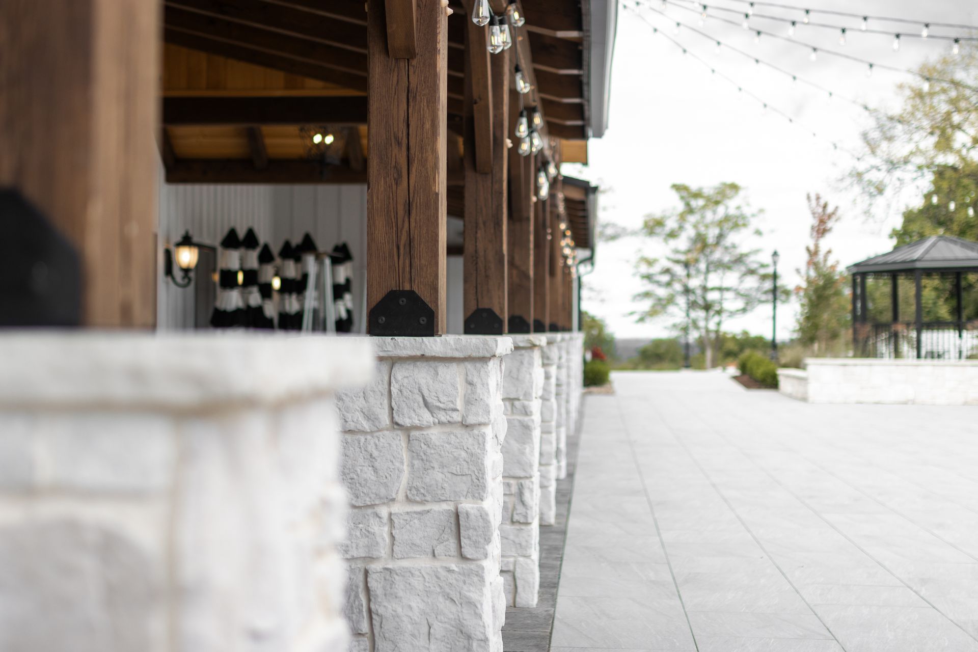 Outdoor patio with white stone walls, wooden posts, string lights, and a paved walkway