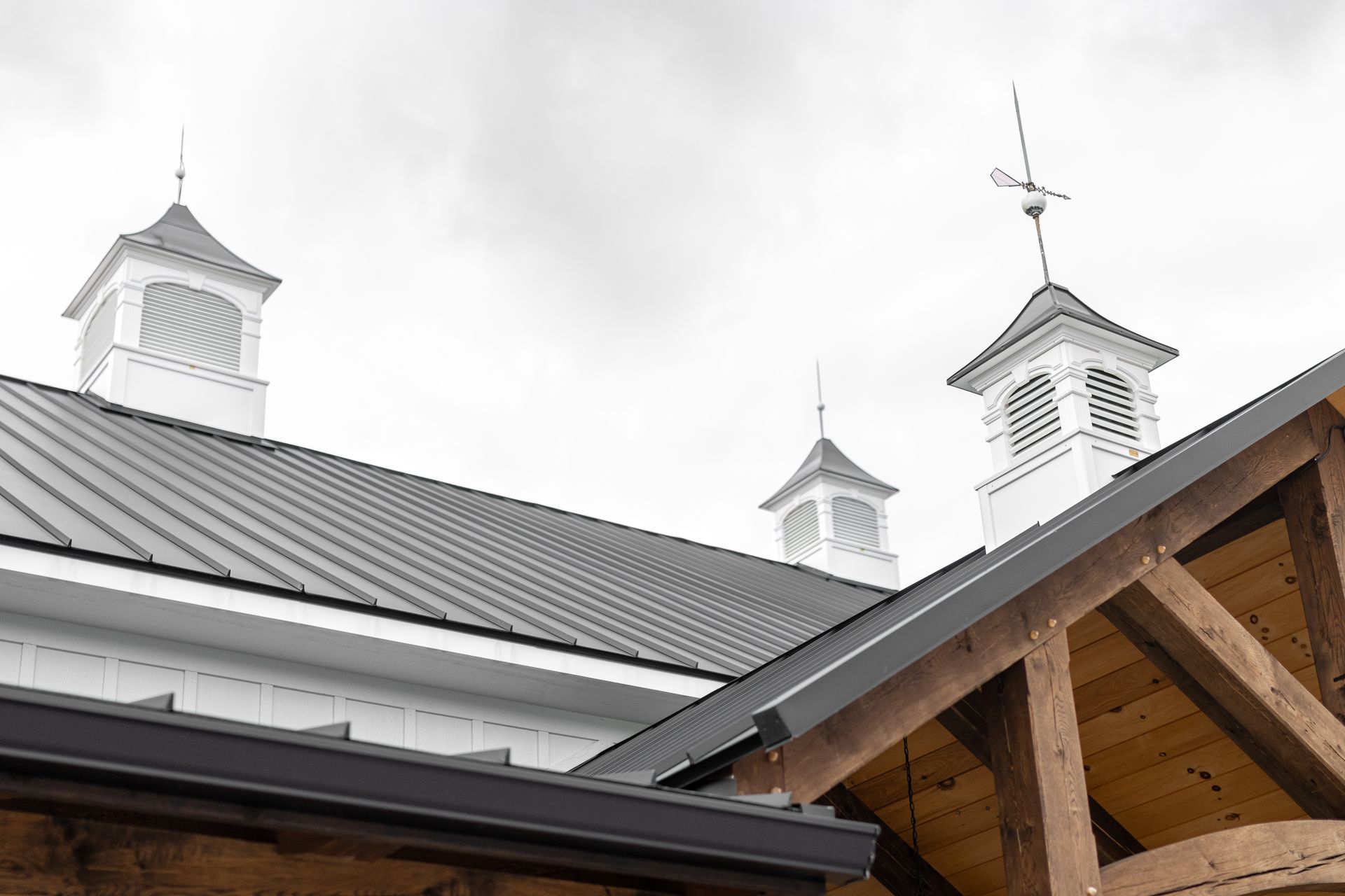 White barn rooftops and cupolas under a cloudy sky, with a wooden gable in the foreground