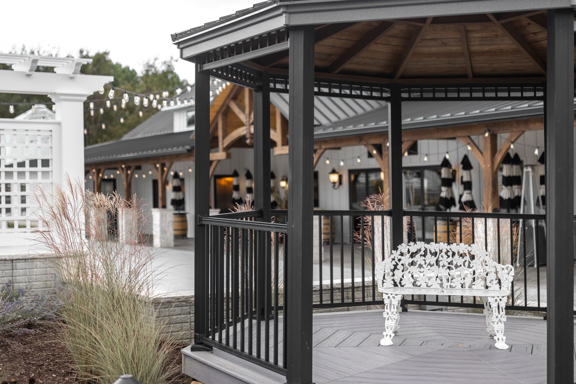 Covered outdoor pavilion with black railings, wooden beams, and a white bench on a gray deck.