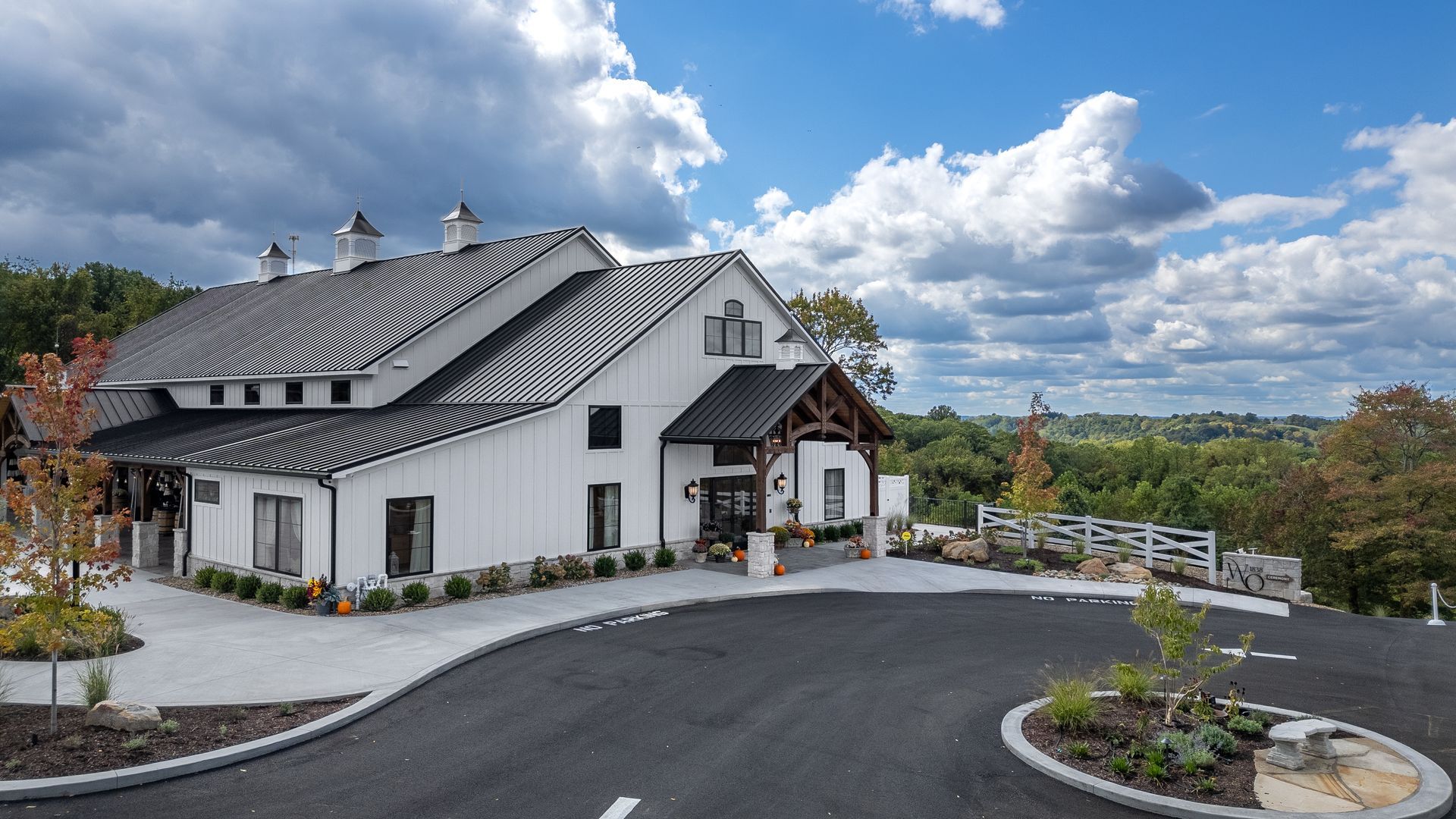 White building with striped roof beside a paved driveway and landscaped garden under a cloudy sky
