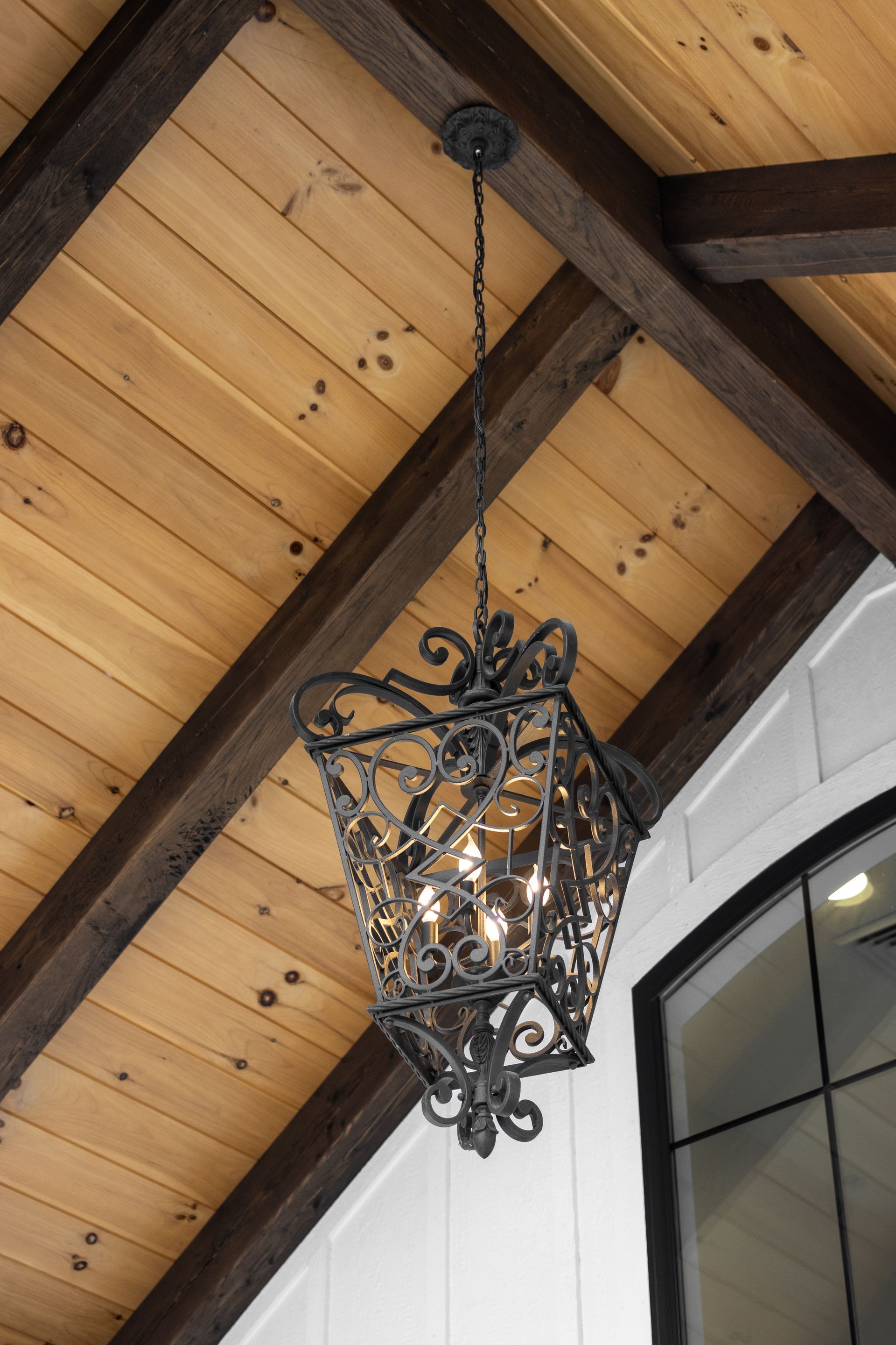 Ornate black hanging chandelier on a wood-paneled vaulted ceiling above an arched window