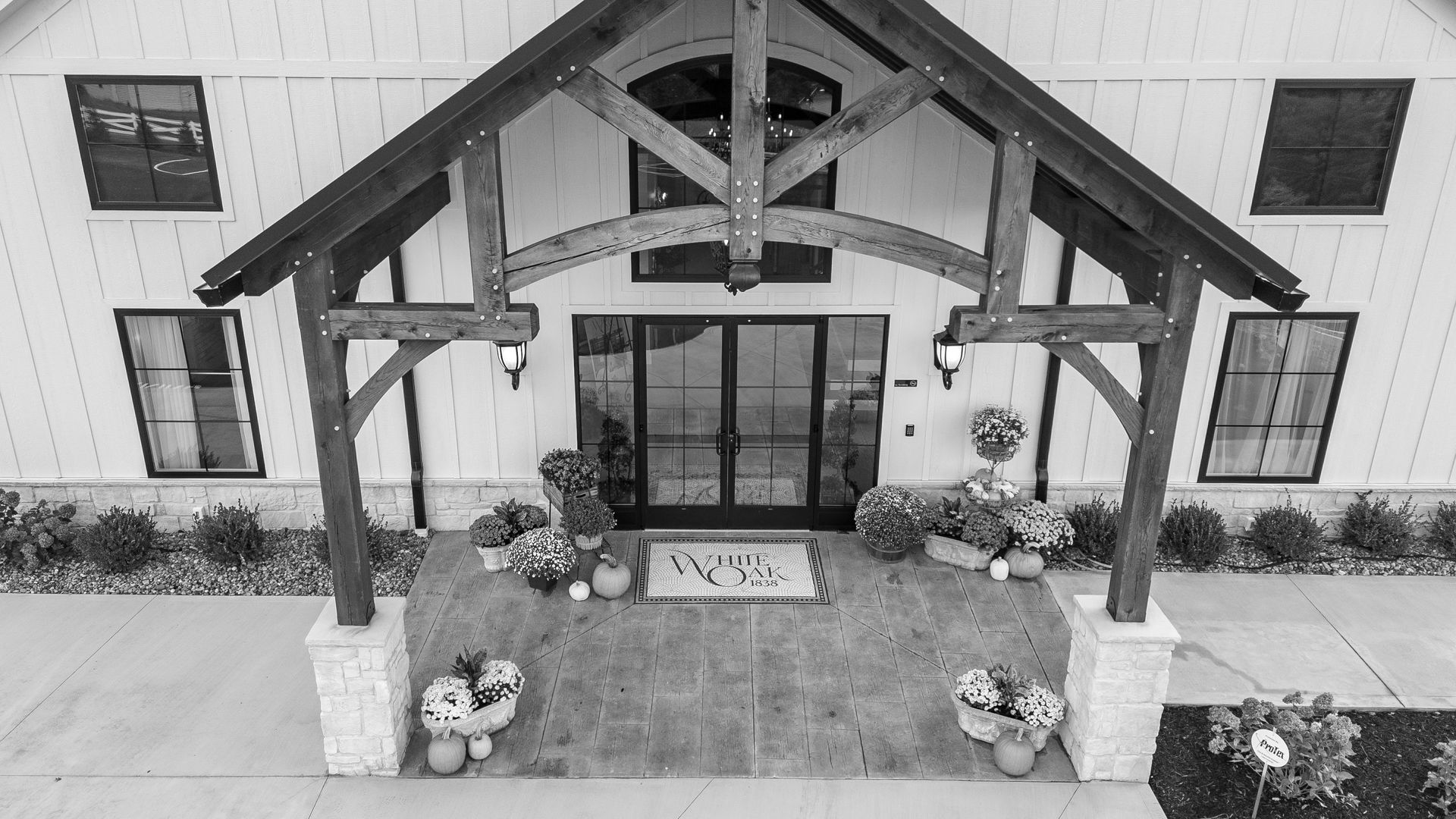 Covered porch entrance with stone steps, wooden beams, potted flowers, and a glass double door