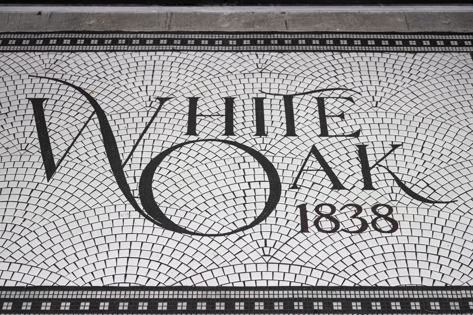 White Oak 1838 logo on a black-and-white mosaic tiled floor border