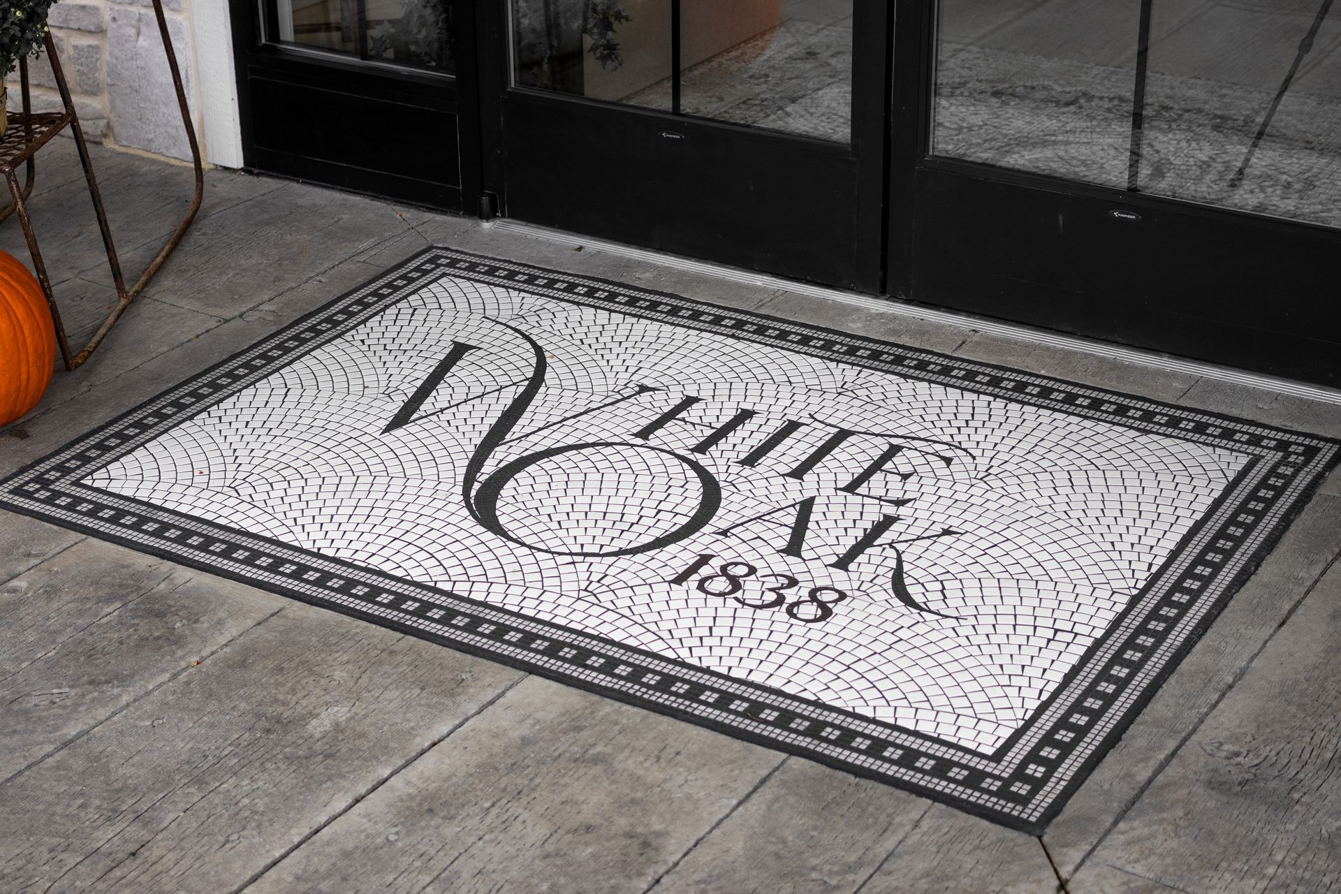 Welcome mat with ornate black script on a white rectangular rug by a glass door