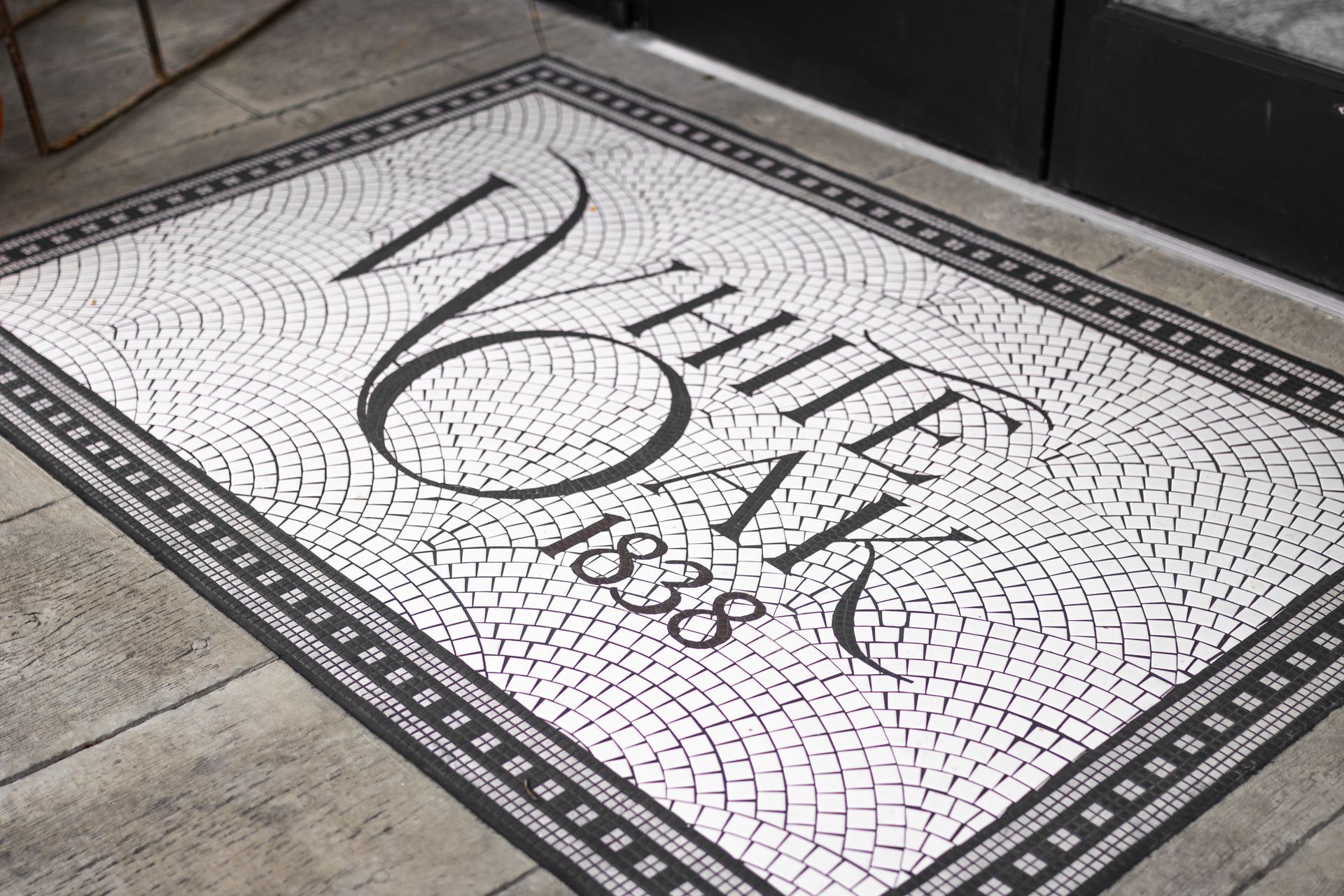 Black-and-white mosaic floor tile with stylized script and a decorative border at an entrance