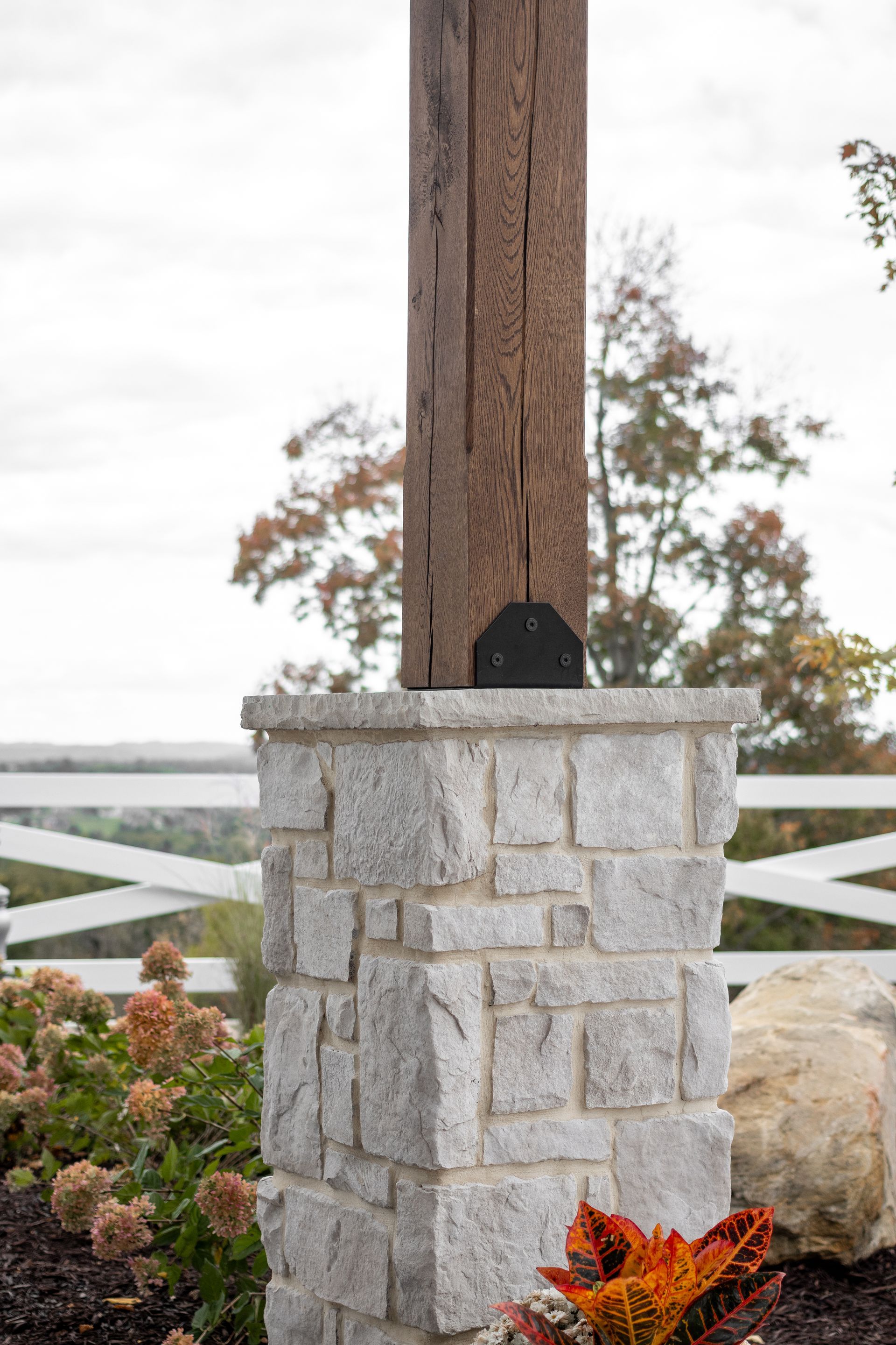 Gray stone pillar with a wooden post, white fence, and autumn flowers by the water