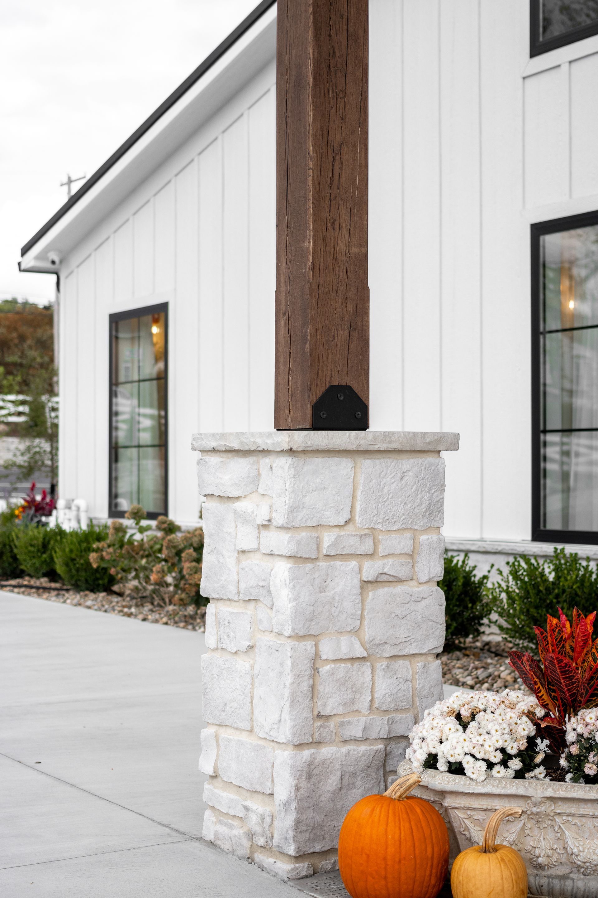 White building entrance with stone pillar, white flowers, and an orange pumpkin by the walkway