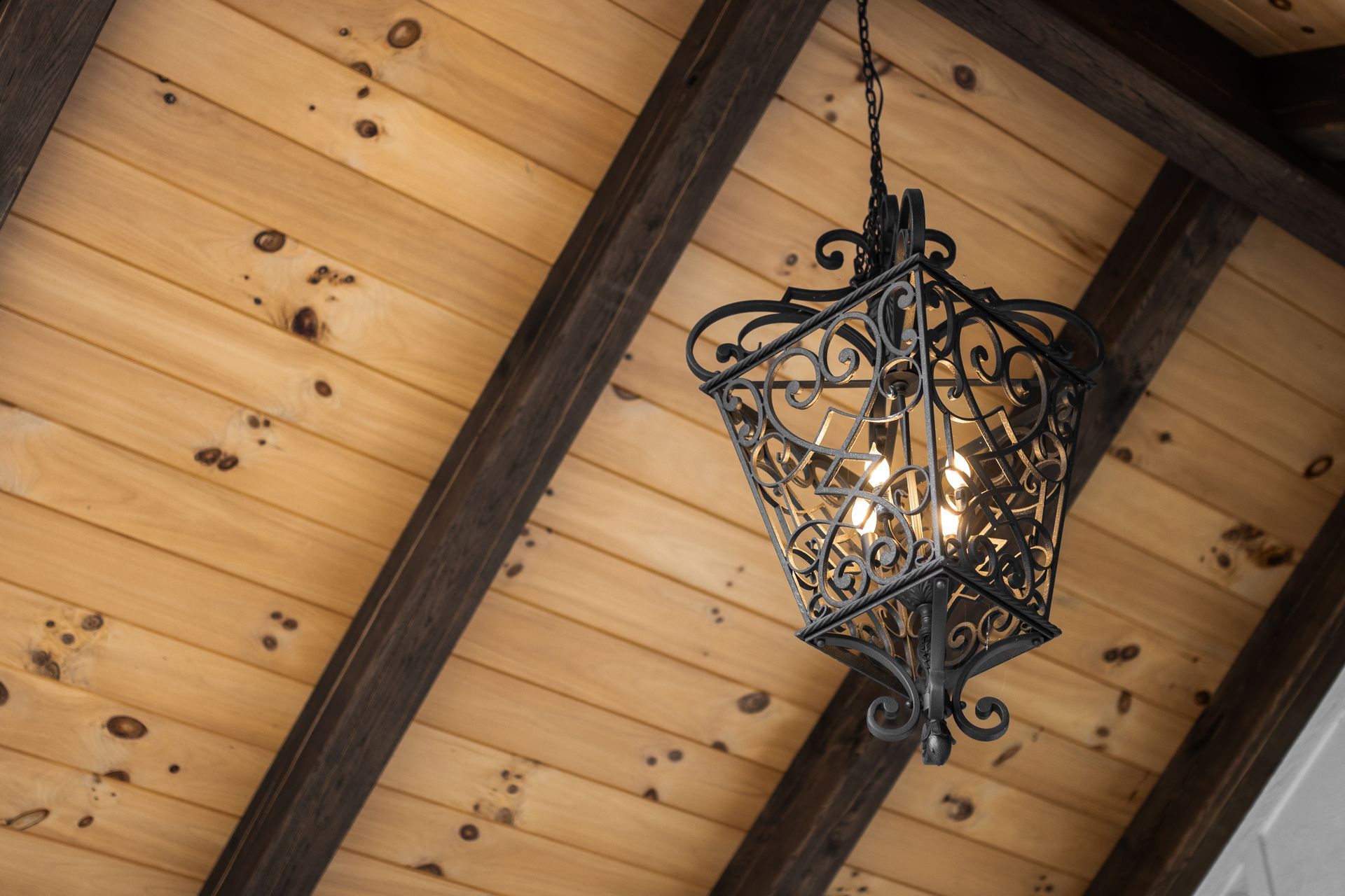 Ornate black hanging lantern on a wood plank ceiling with dark beams and warm light