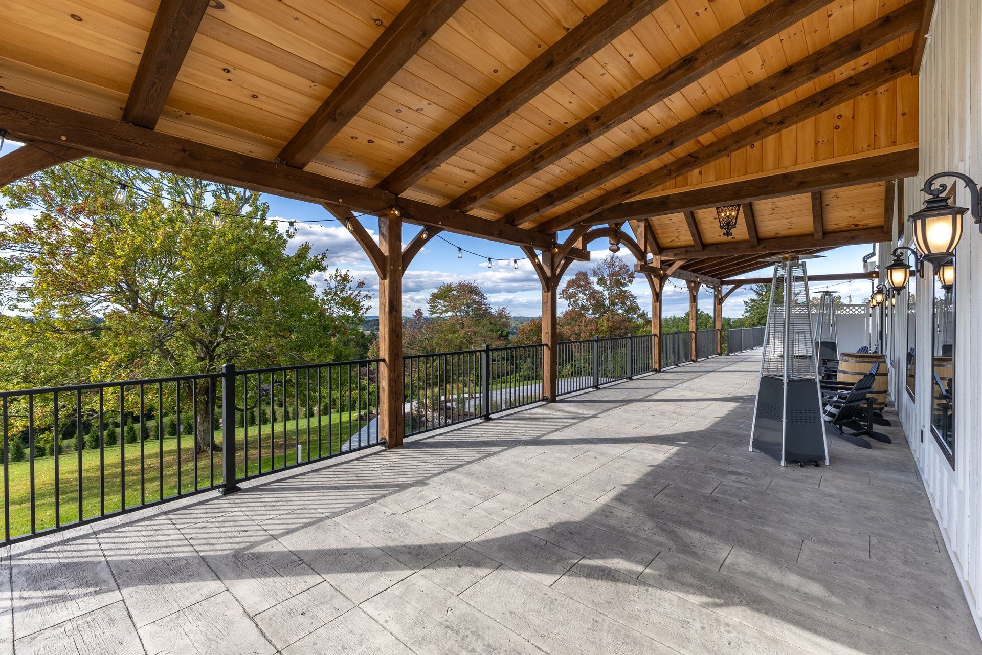 Covered outdoor patio with wooden ceiling, black railing, and a scenic view beyond the trees
