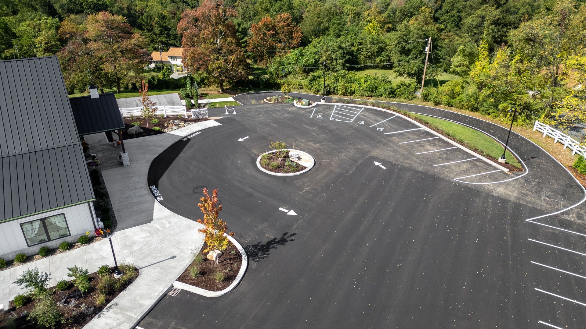 Curved asphalt parking lot beside a gray building, with landscaped islands and trees in autumn colors
