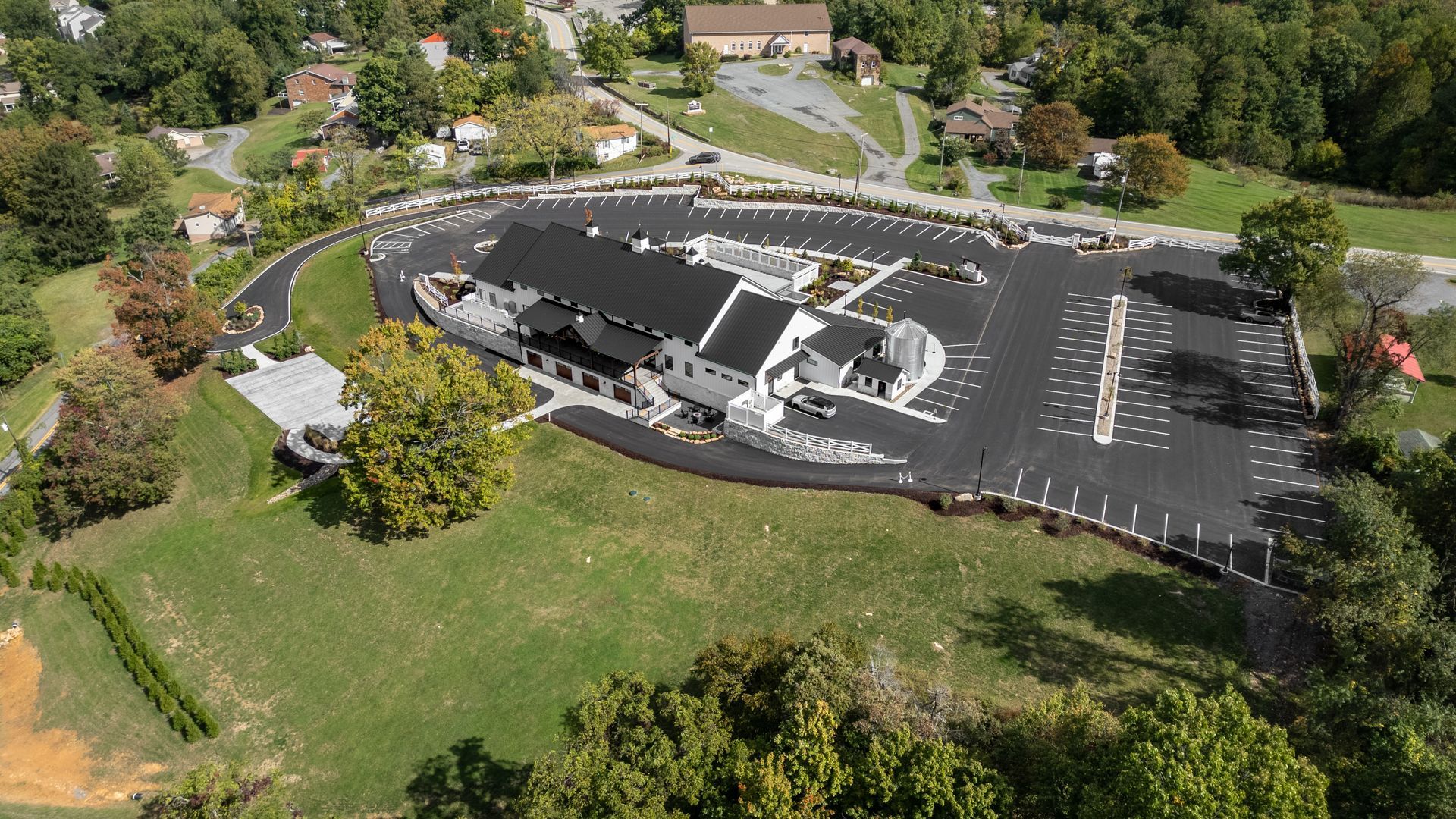 Aerial view of a black-roofed building with parking lot, surrounded by trees and grass.