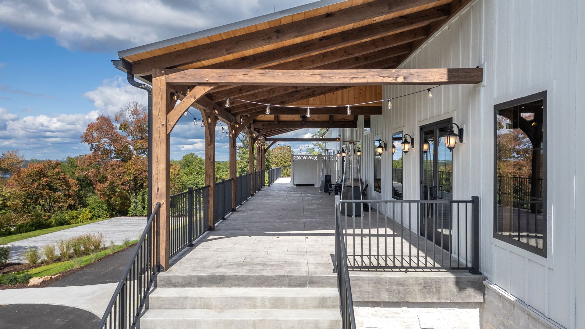 Covered walkway with wooden beams, stairs, and railings beside a white building in a sunny outdoor setting