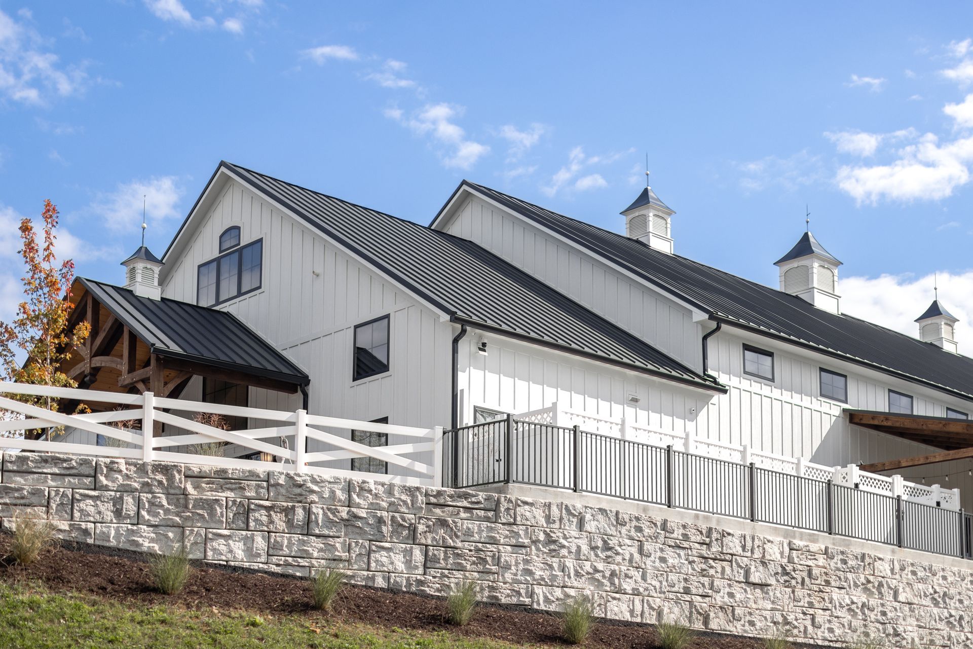 White barn-like building with gray roof and fence on a stone wall under a blue sky