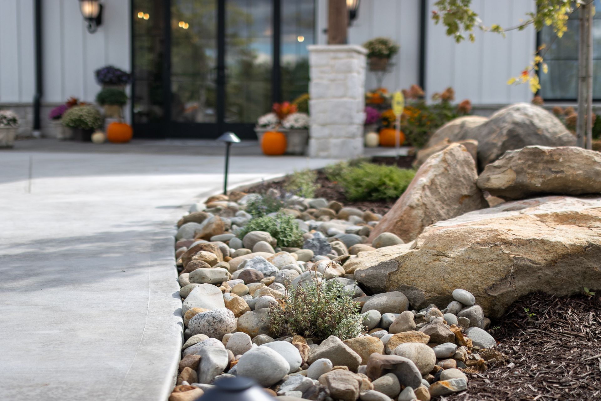 Rock garden with large boulders, pebbles, and low plants beside a modern building entrance