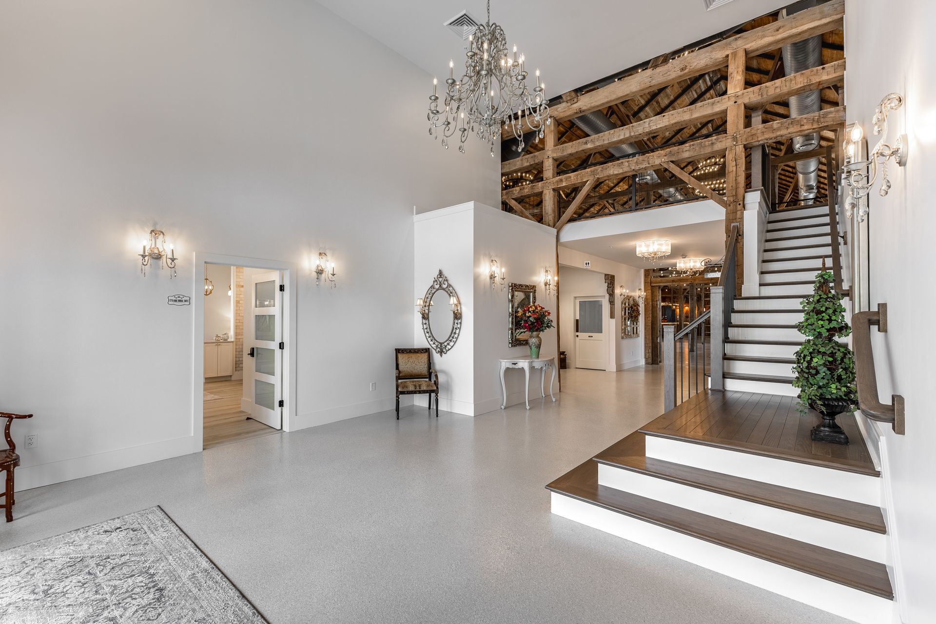 Bright, modern foyer with staircase, chandelier, mirror, white walls, and wood loft railing