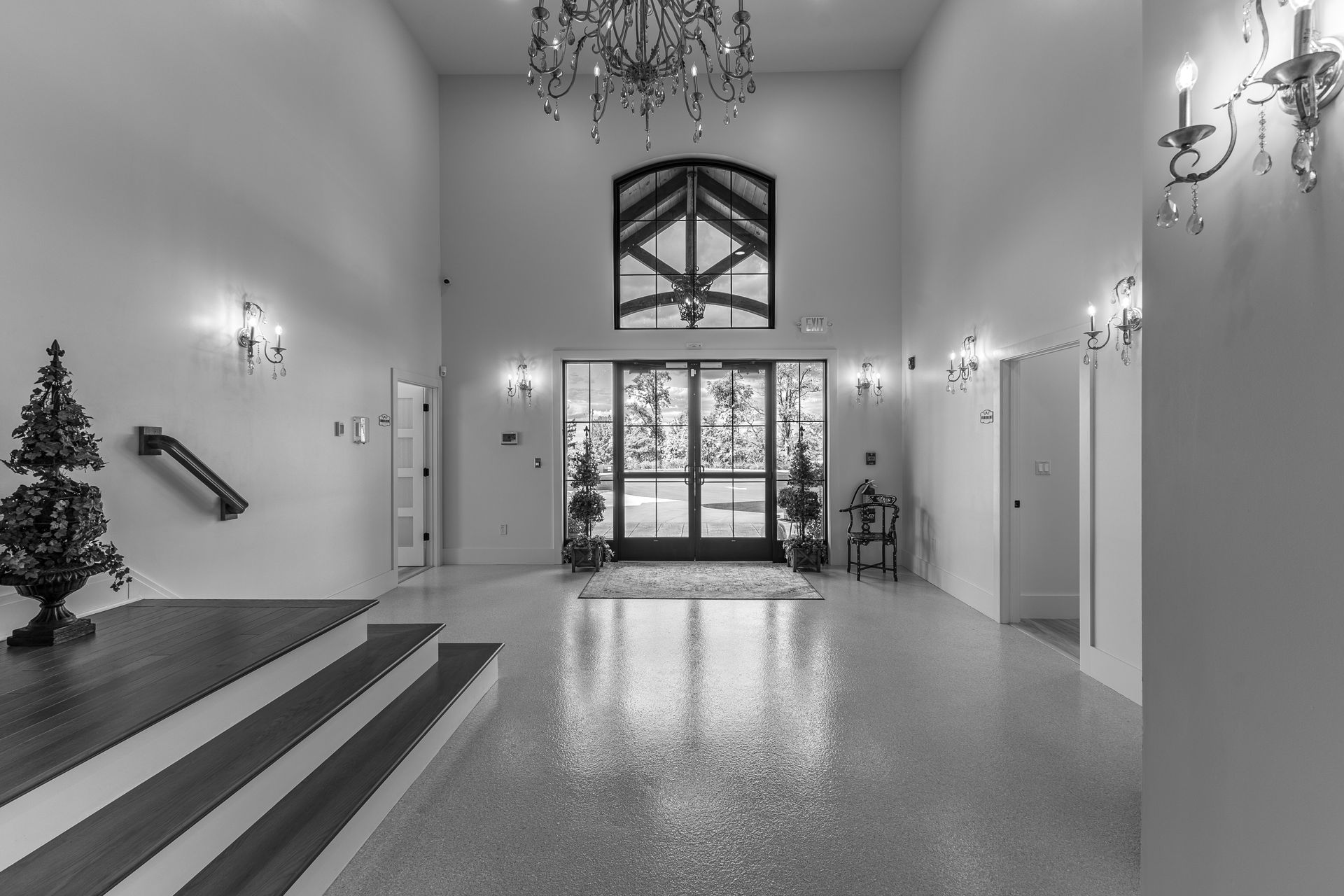 Spacious lobby with chandelier, large glass entry doors, staircase, and decorated Christmas tree.