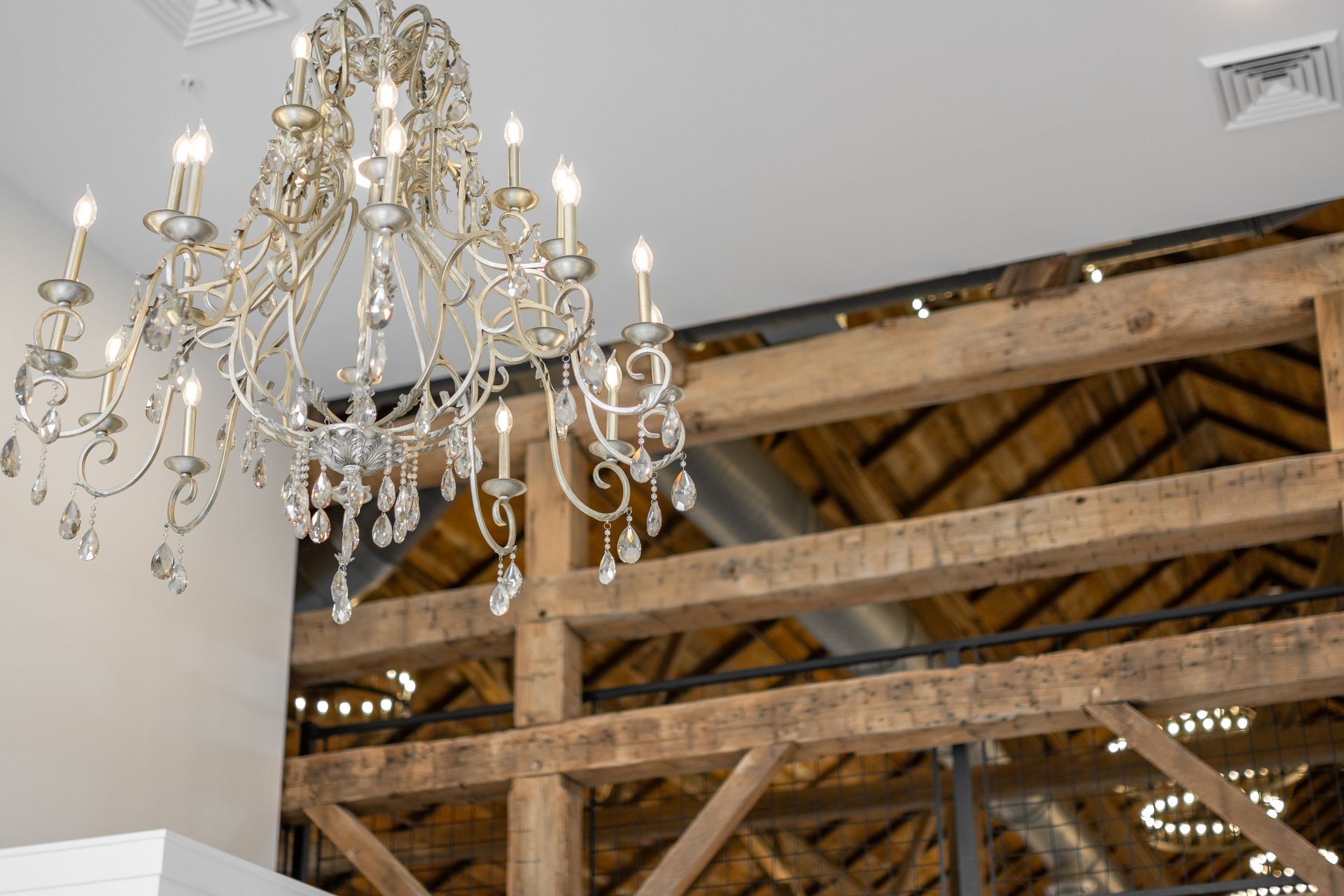 Ornate chandelier hanging from a rustic wooden-beamed ceiling in a bright interior