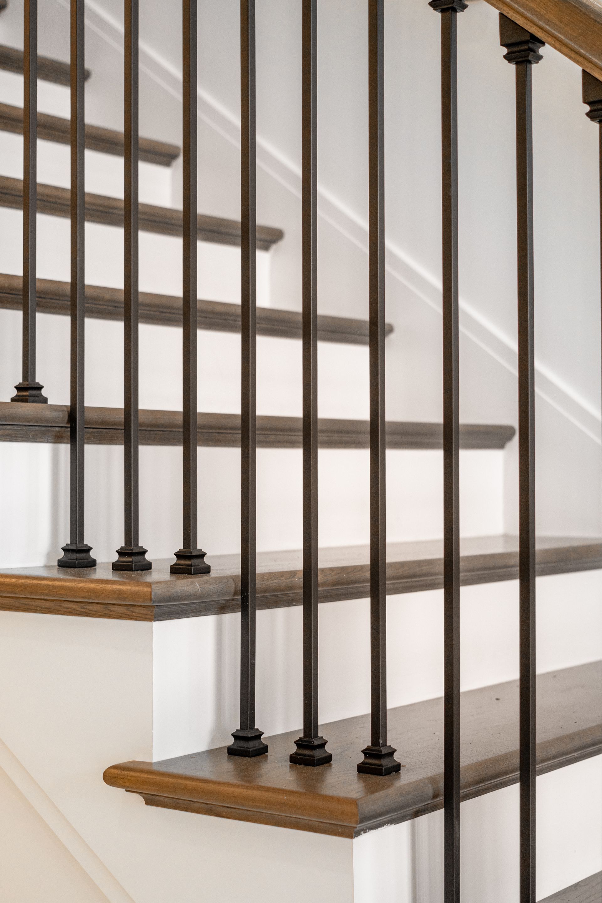 Staircase with white steps, dark wooden treads, and black metal balusters against a white wall