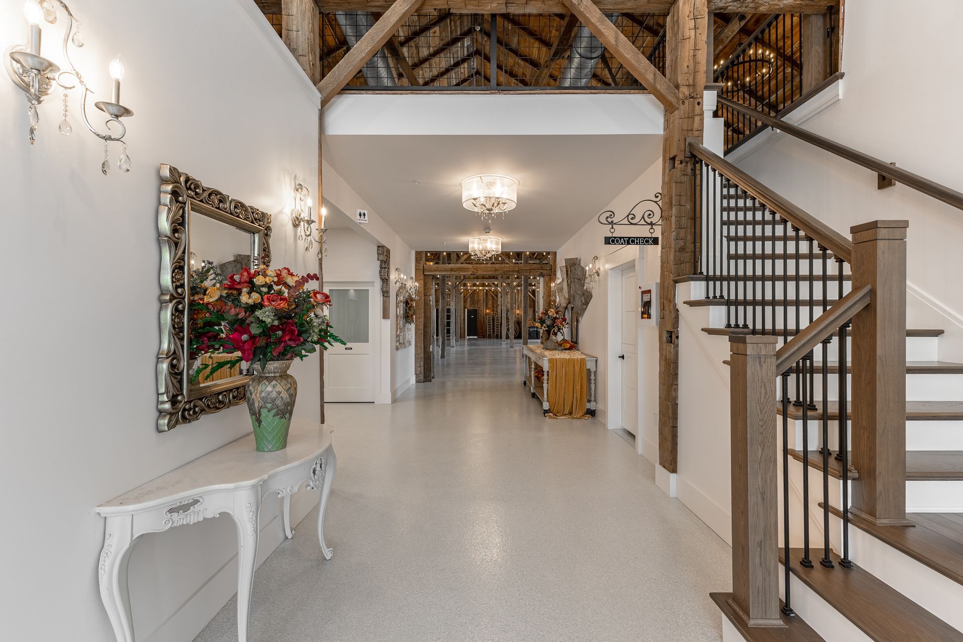 Bright foyer with staircase, white console table, floral arrangement, and chandelier lighting