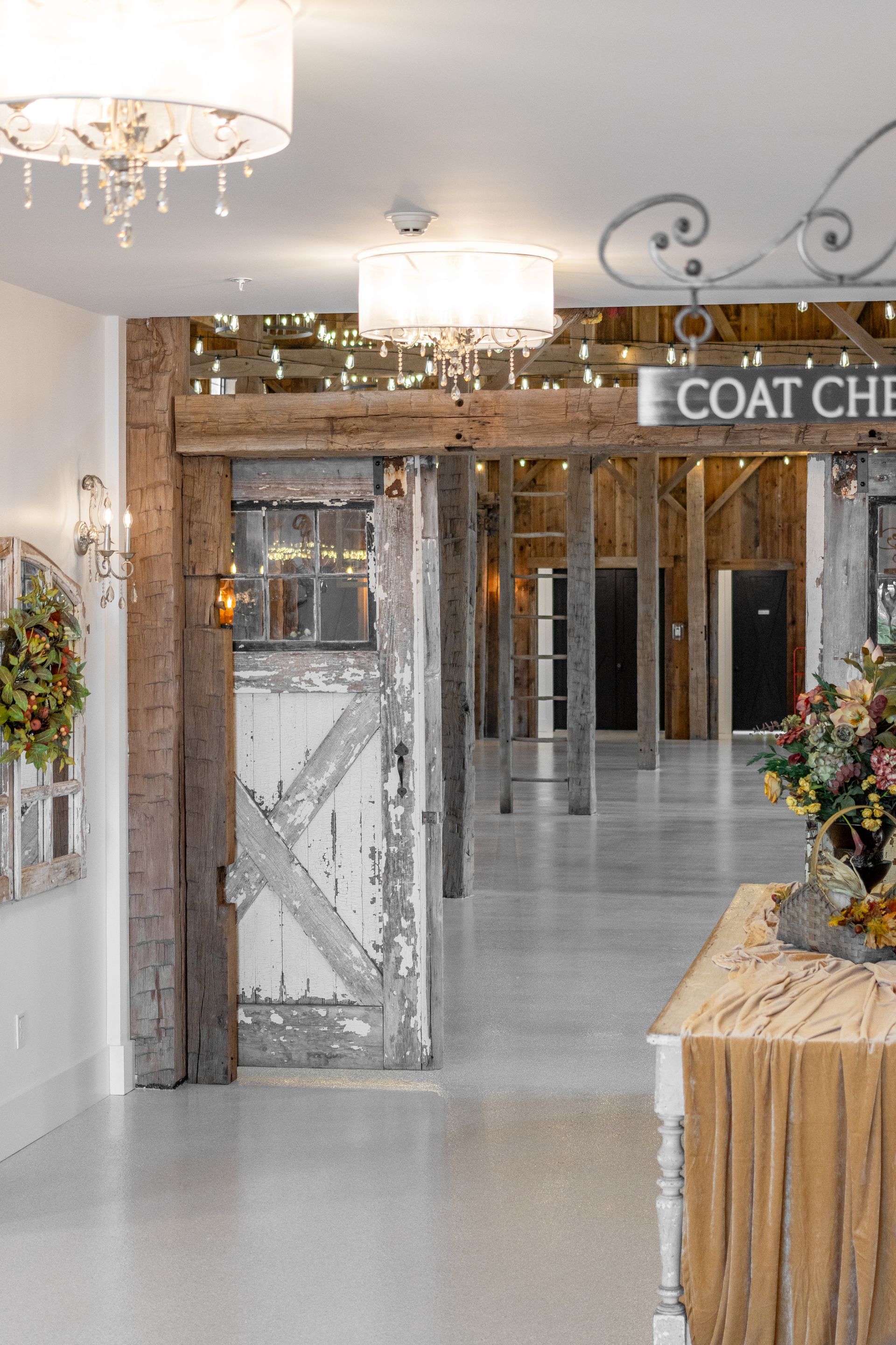 Bright lobby entrance with glass doors, chandeliers, and a coat check sign above floral arrangements