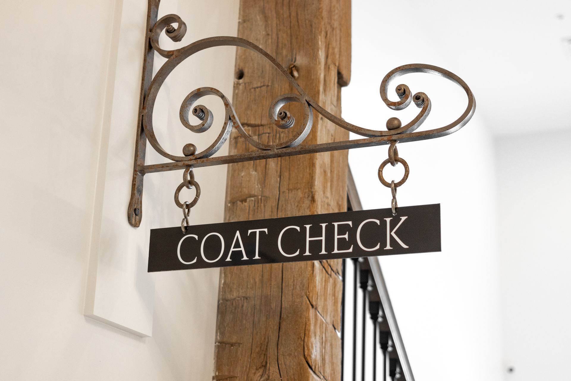Ornate black metal “COAT CHECK” sign mounted on a wooden post indoors