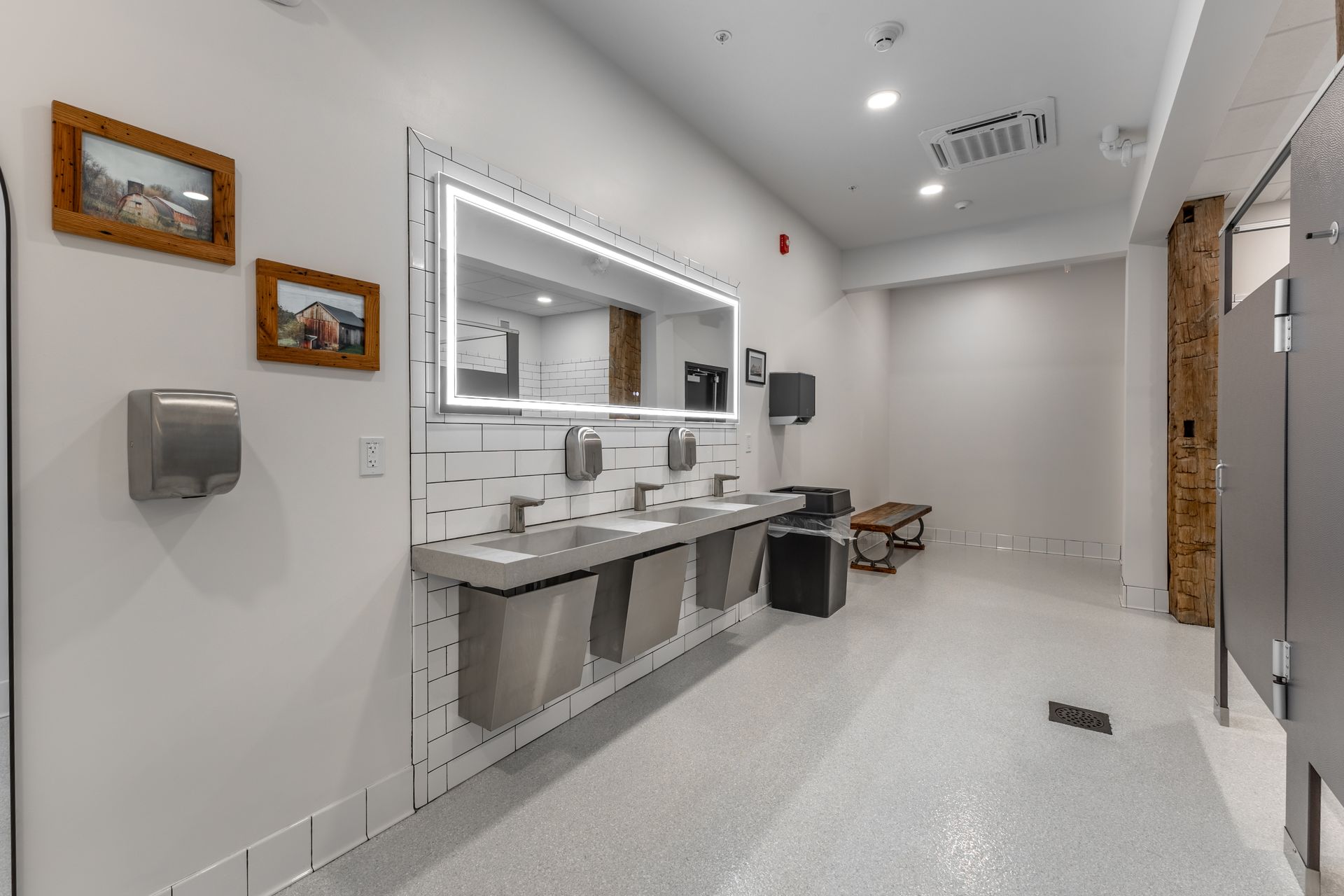 White Oak 1838's restroom with double sinks, mirrors, and white tiled walls; a wooden door is open on the right.