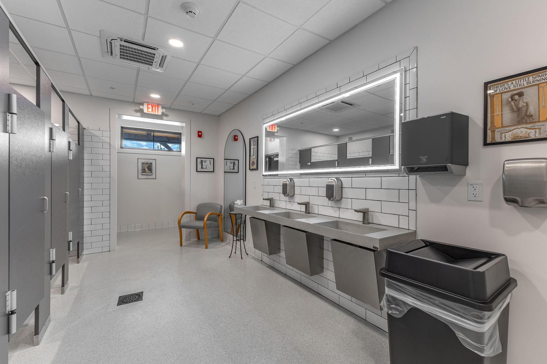 Bright clean restroom with metal counters, sinks, cabinets, and stools under fluorescent lights
