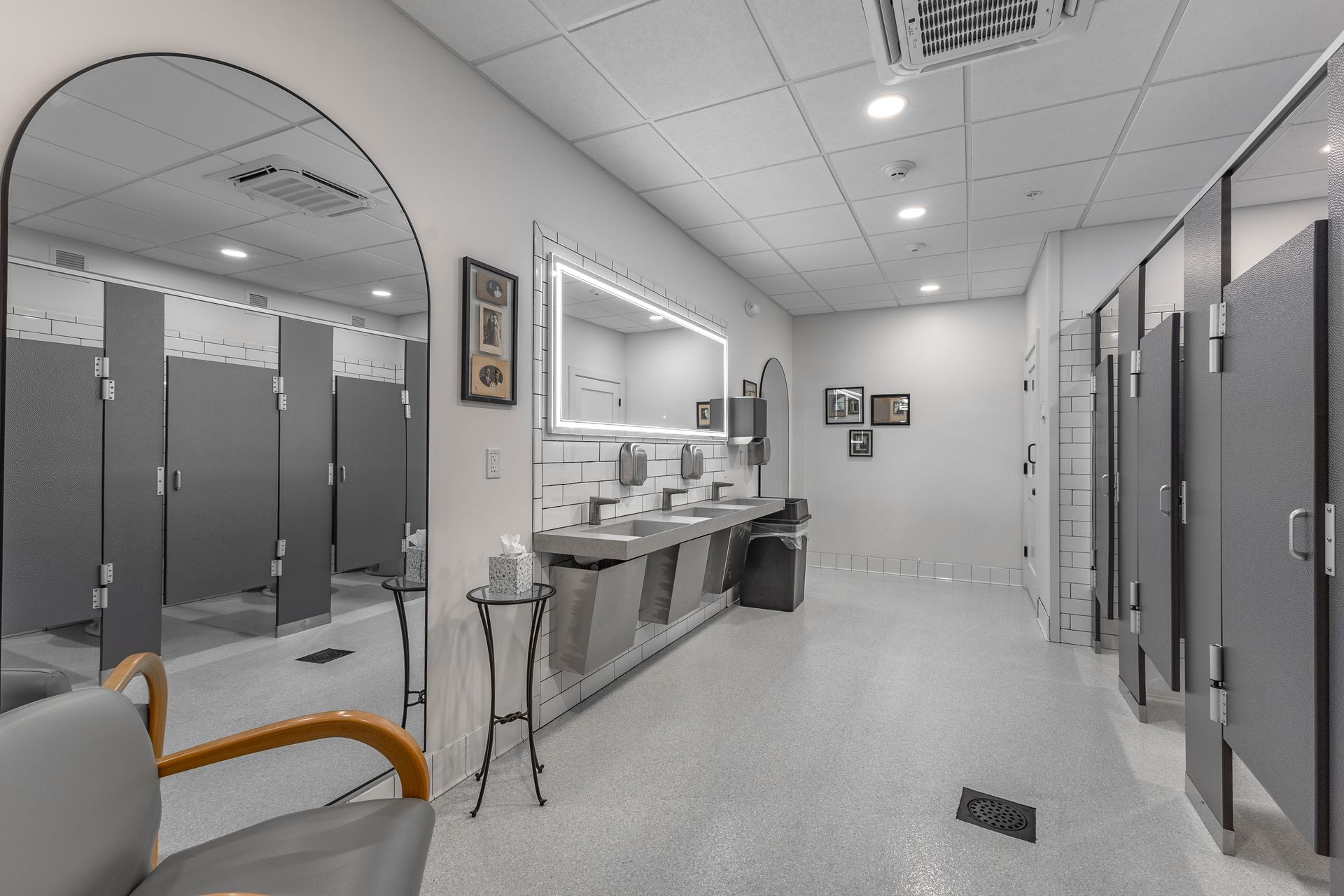 White Oak 1838's restroom with sinks, mirrors, and gray stalls, lit by bright ceiling lights.