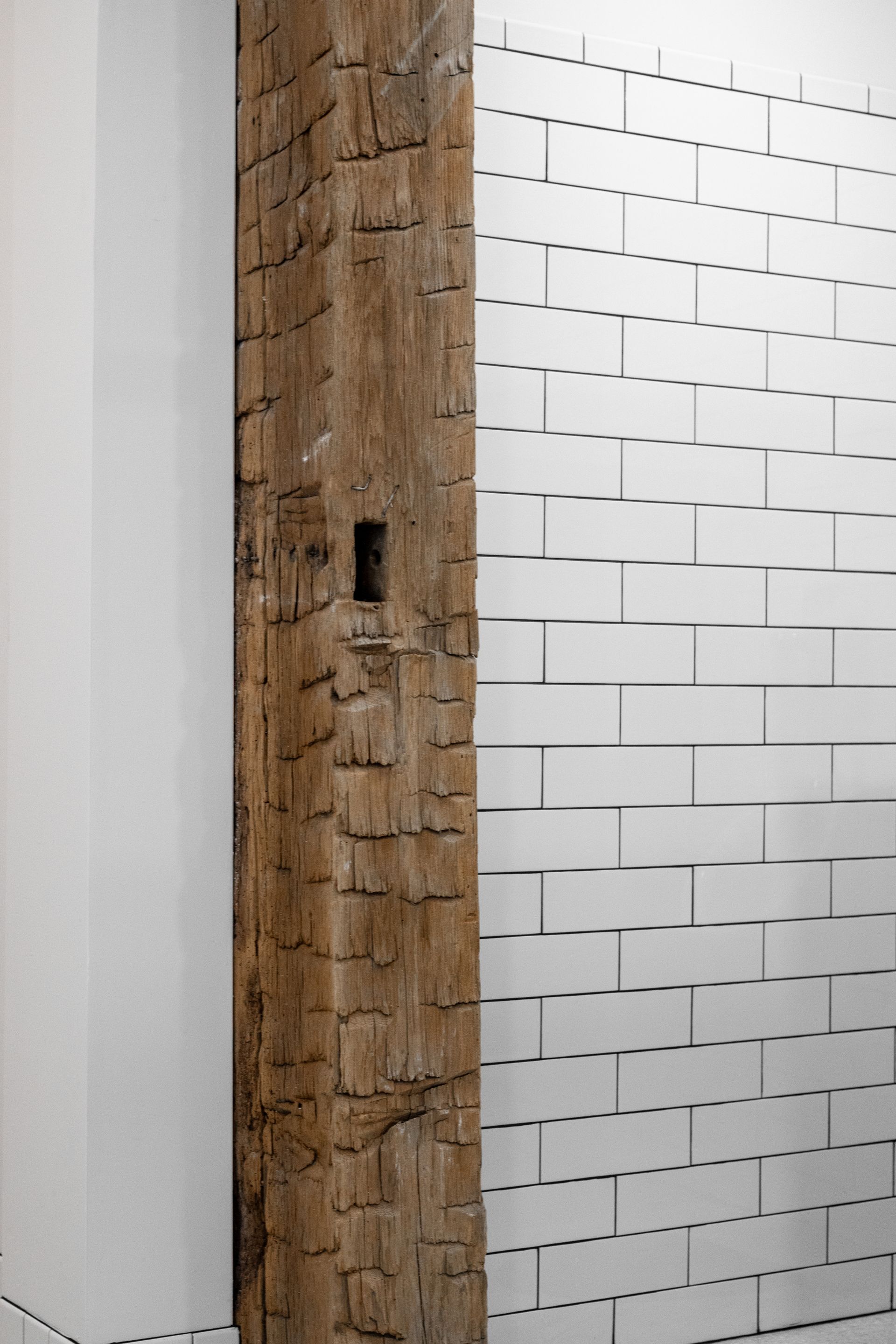 Wooden post beside a white tiled wall with staggered black lines