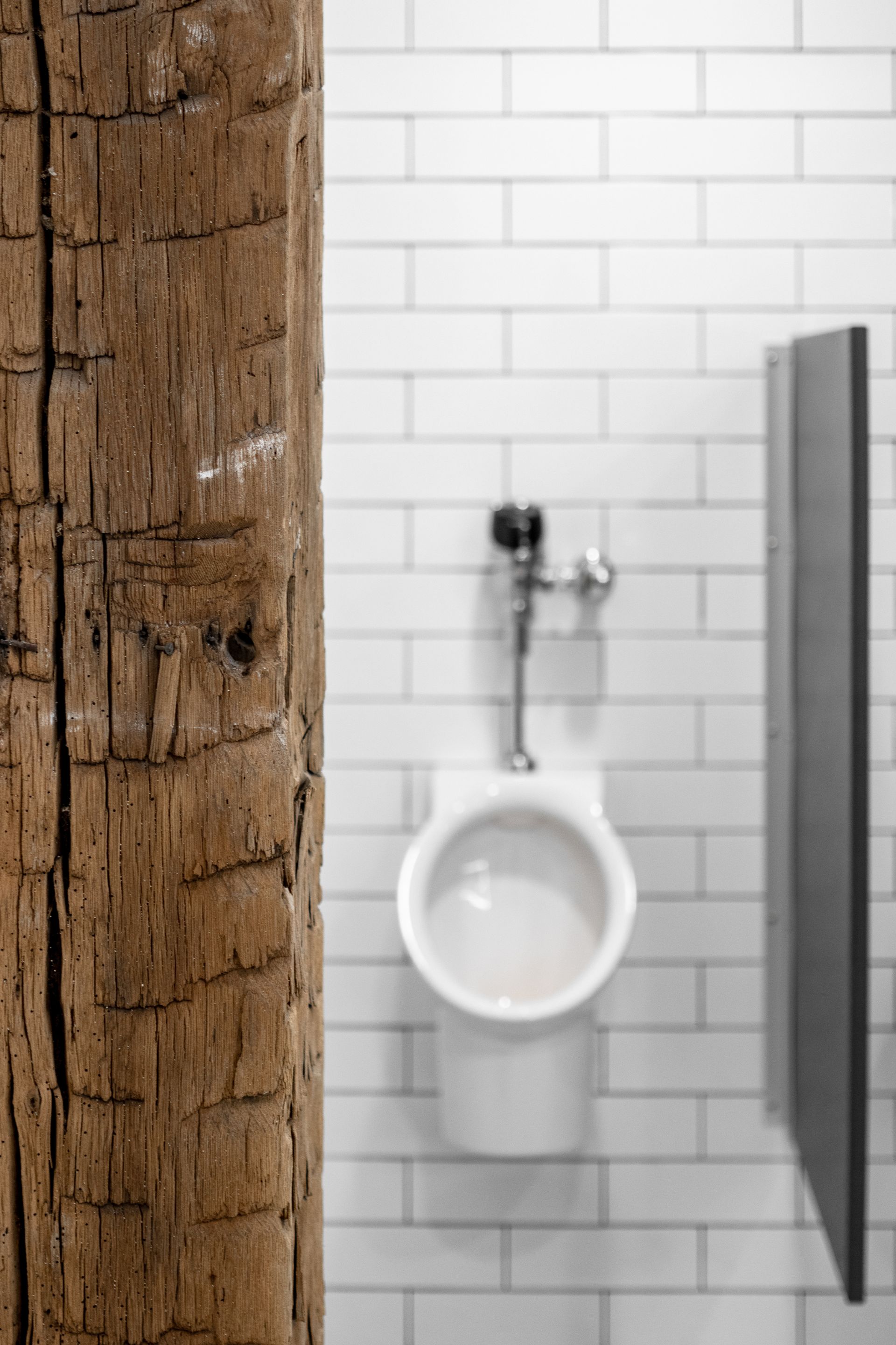 Rustic wood frame bordering a white-tiled restroom wall with a urinal and stall partition visible.