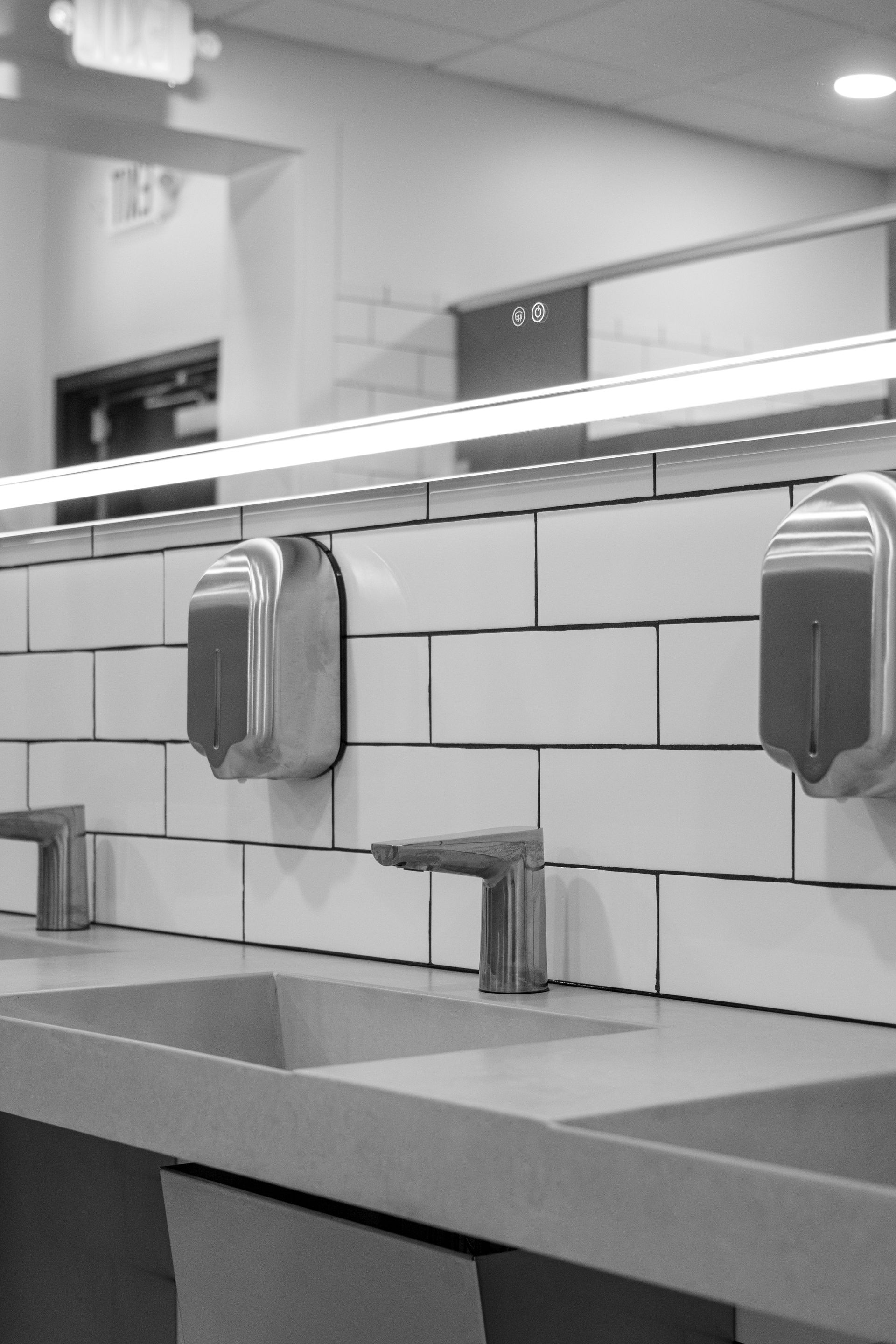 Restroom sink area with mirror, tiled wall, and soap dispensers